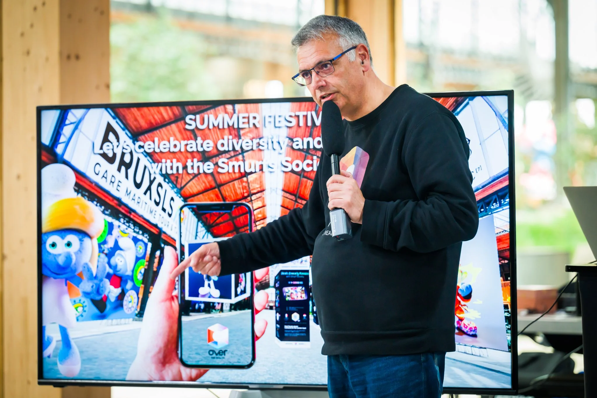 Vincent Parissis speaks into the microphone in front of a screen displaying images of the Smurfs during a press conference at the Gare Maritime in Brussels.