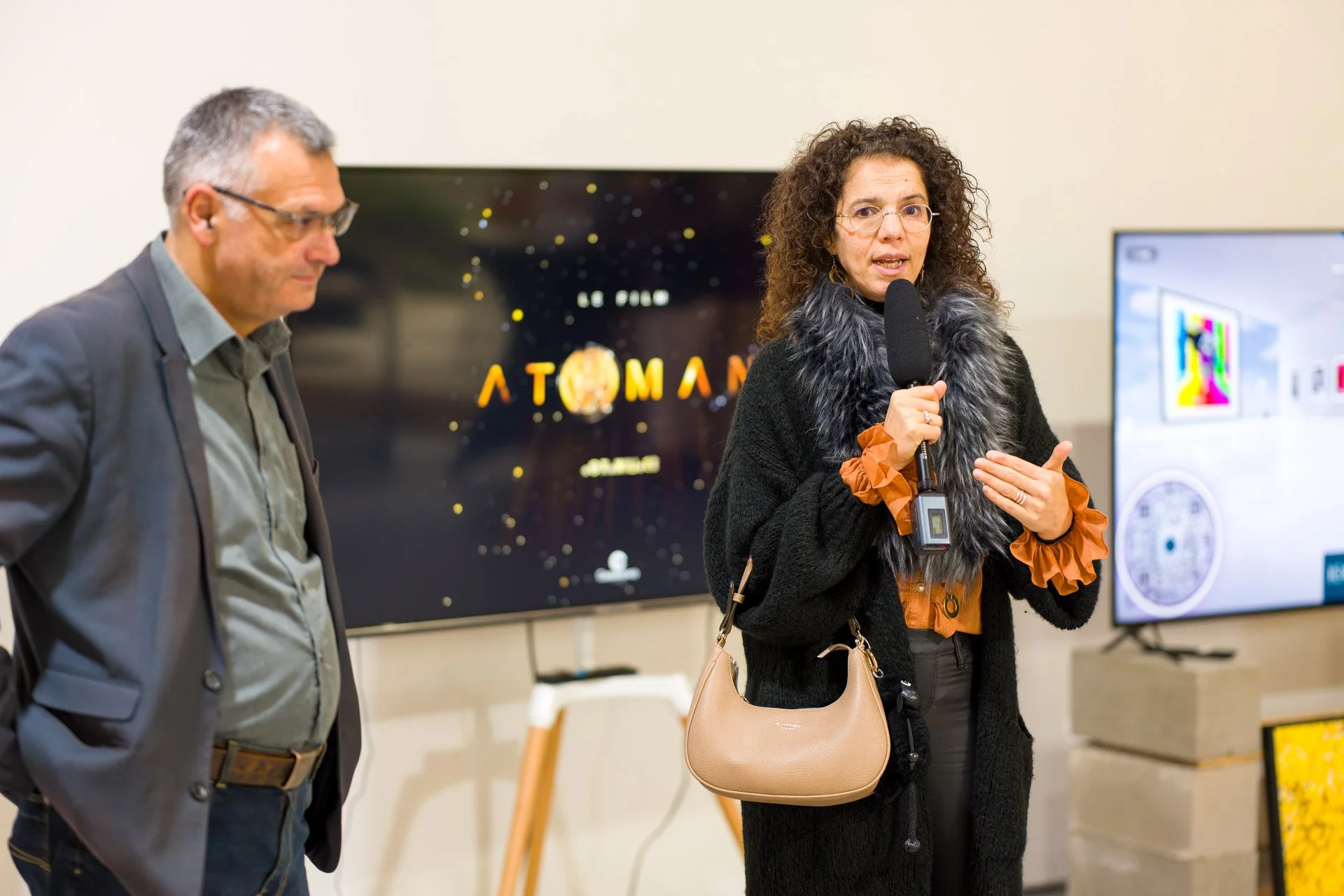 Deux personnes devant un écran affichant "Atoman". L'une parle dans un micro.
