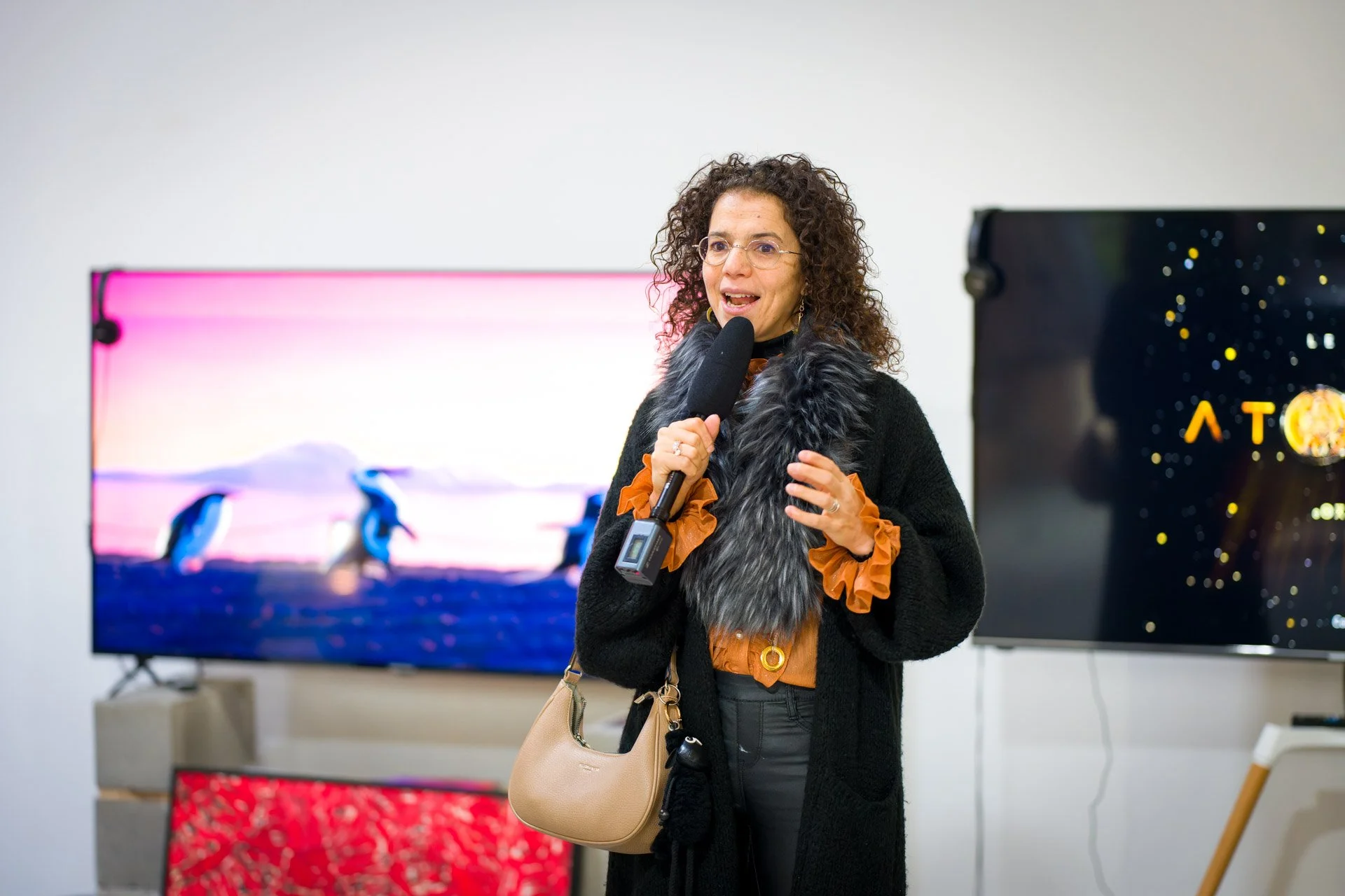 Hanane Risayindi accompagne son intervention de gestes des mains devant des écrans à la BXL ART NFT Gallery.