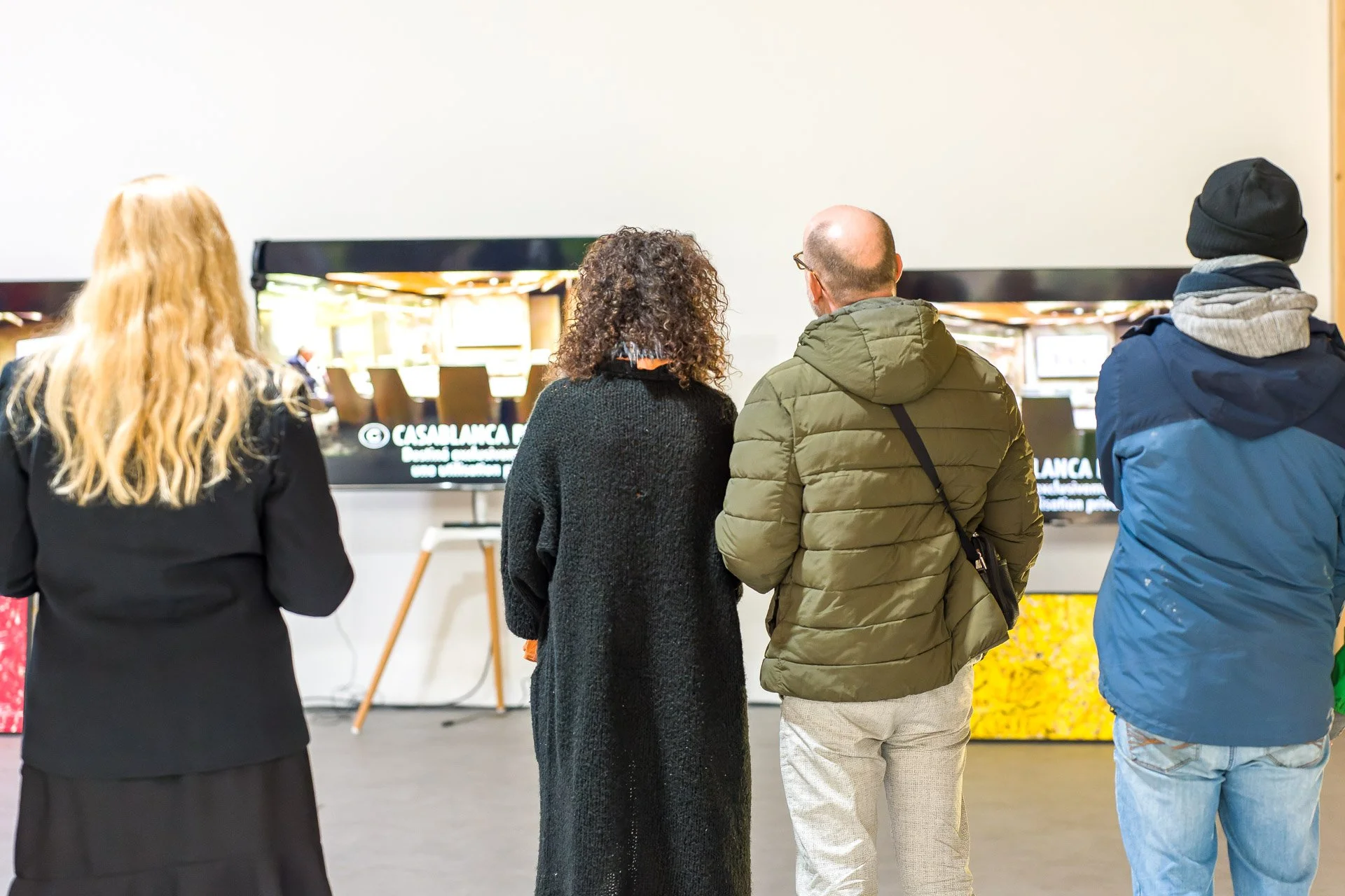 Groupe de personnes regardant un écran dans une galerie ou exposition.