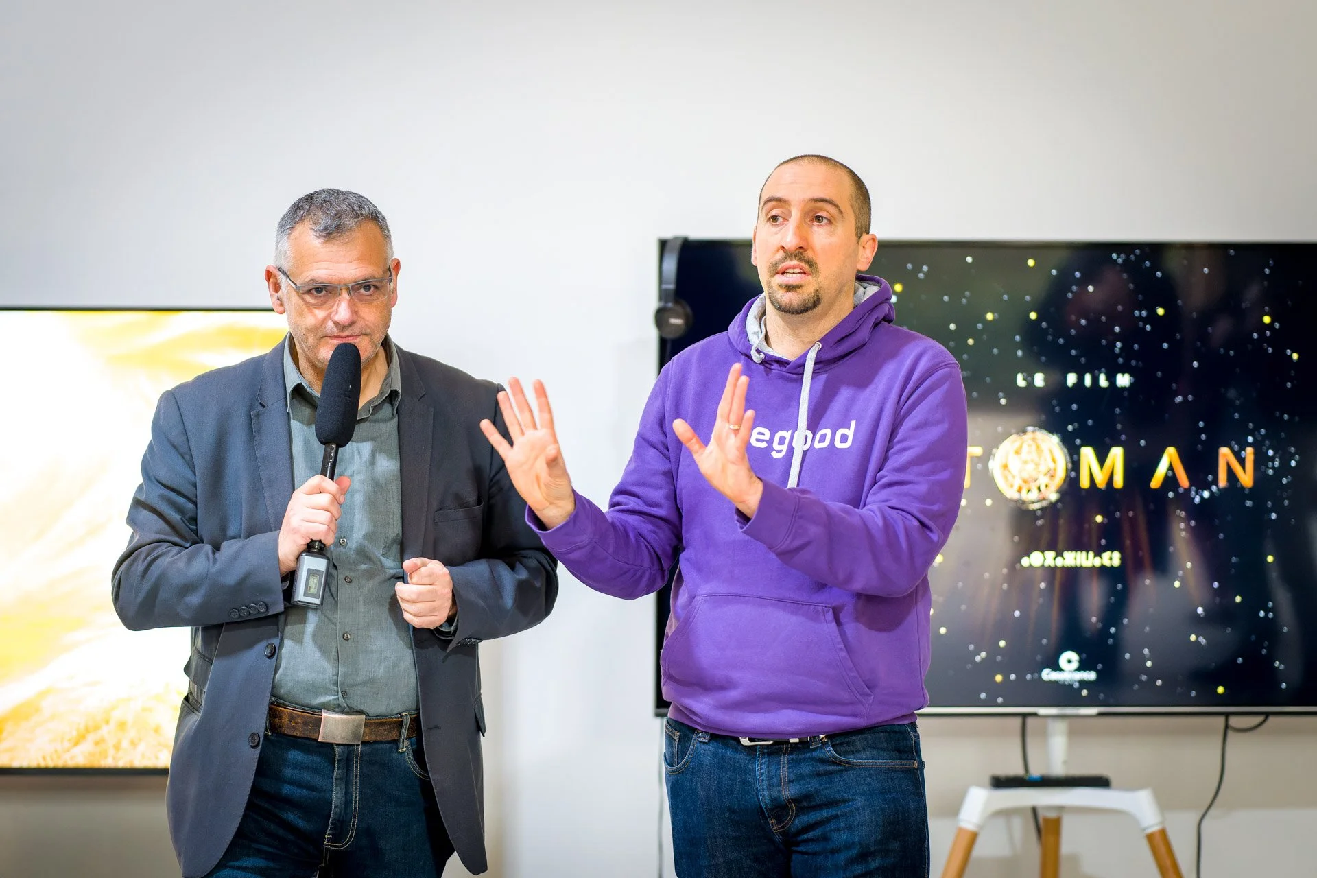 Vincent Parissis et Grégory Monfort s’expriment au microphone devant des écrans lors d’un événement à la BXL ART NFT Gallery.