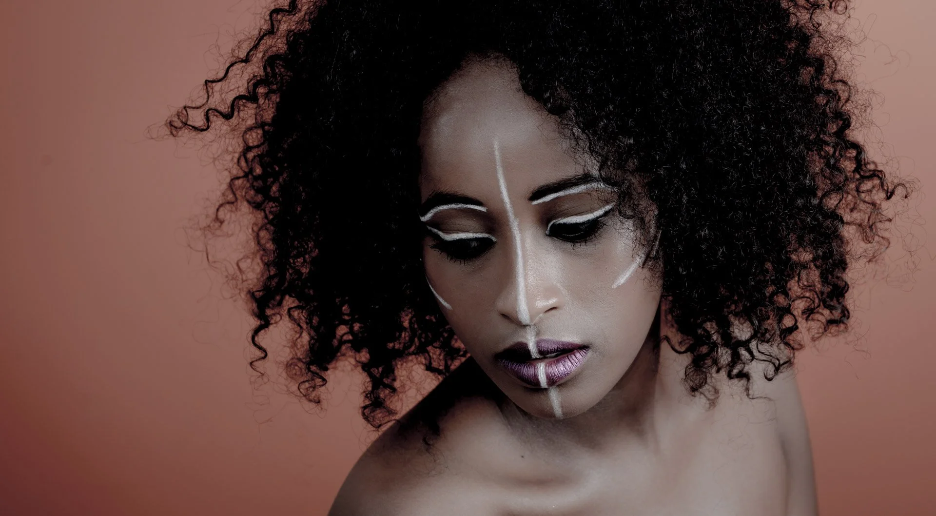 Femme avec maquillage tribal et cheveux bouclés sur fond orange.
