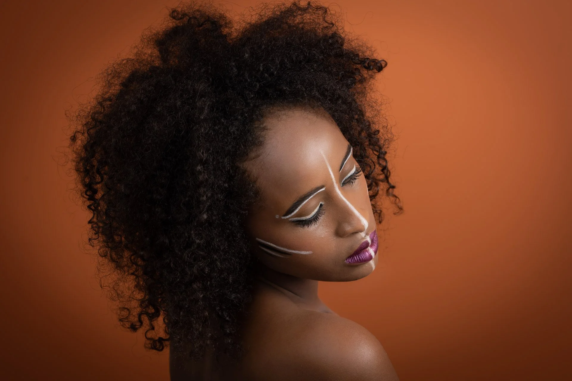 Femme de profil avec maquillage artistique et cheveux bouclés sur fond orange.