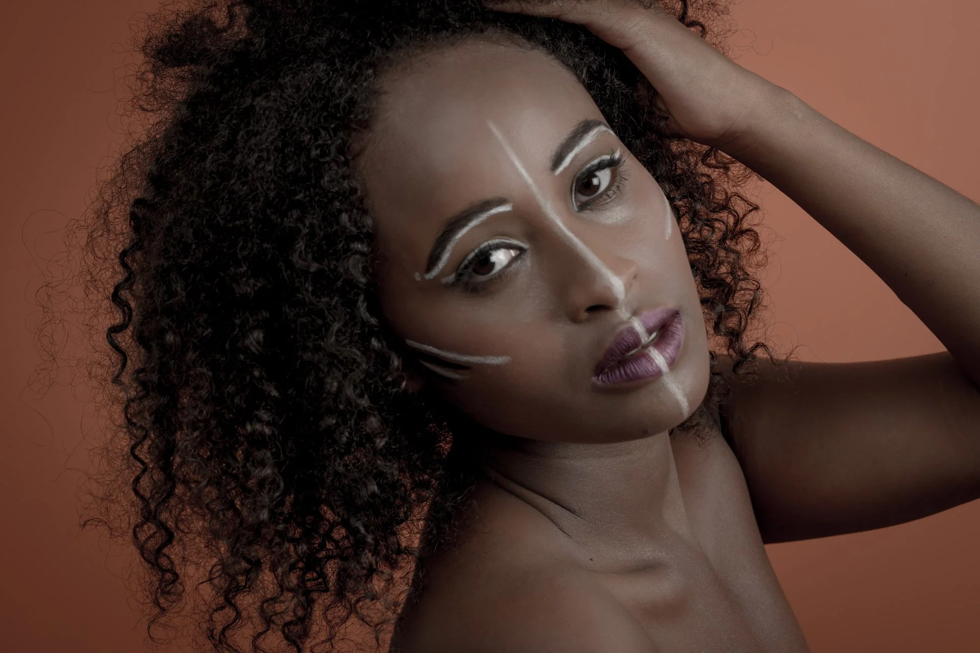 Femme avec du maquillage artistique sur le visage et fond orange.