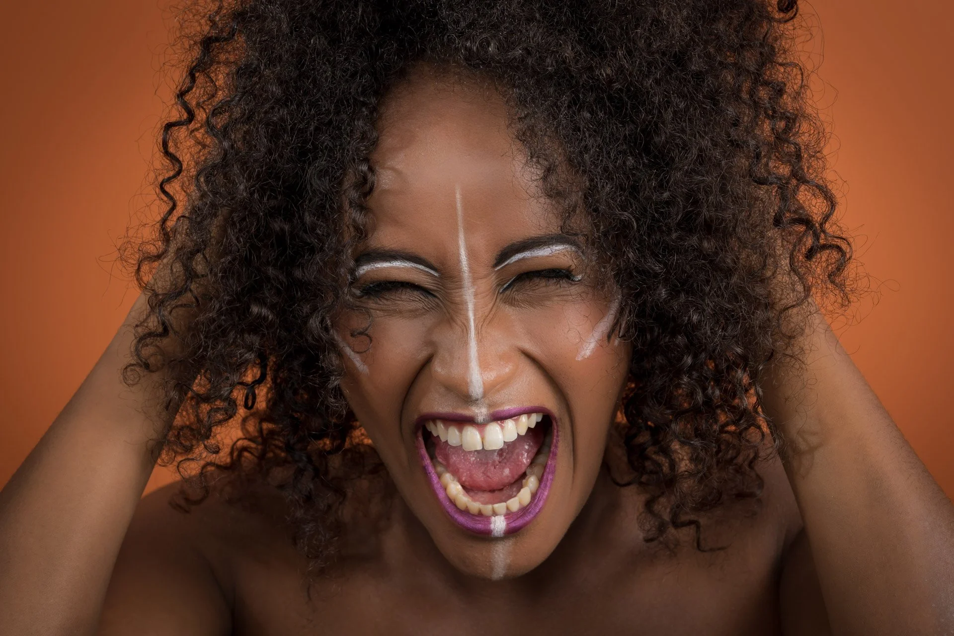 Personne criant avec des marques de peinture blanche sur le visage, fond orange.
