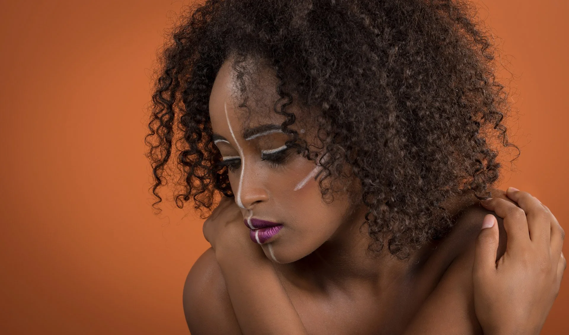 Femme avec des cheveux bouclés et maquillage artistique sur fond orange.