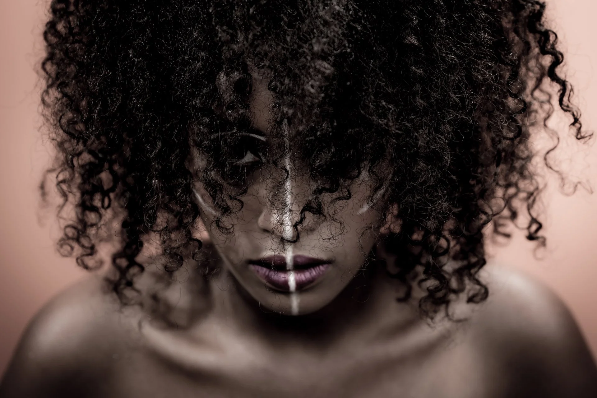 Une personne avec les cheveux bouclés regardant vers le bas, portant du maquillage blanc sur le visage.