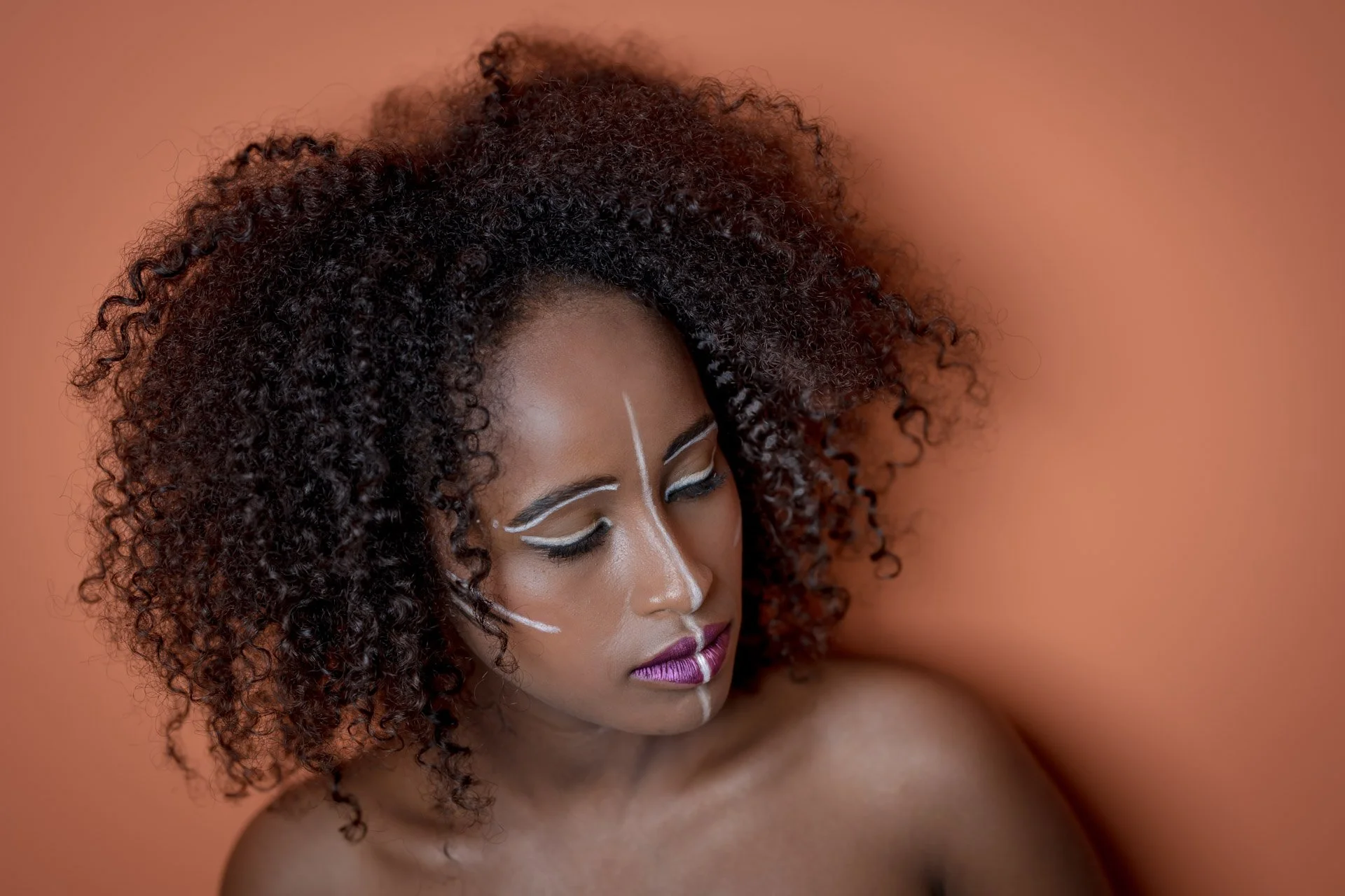 Femme aux cheveux bouclés avec maquillage artistique sur fond orange.