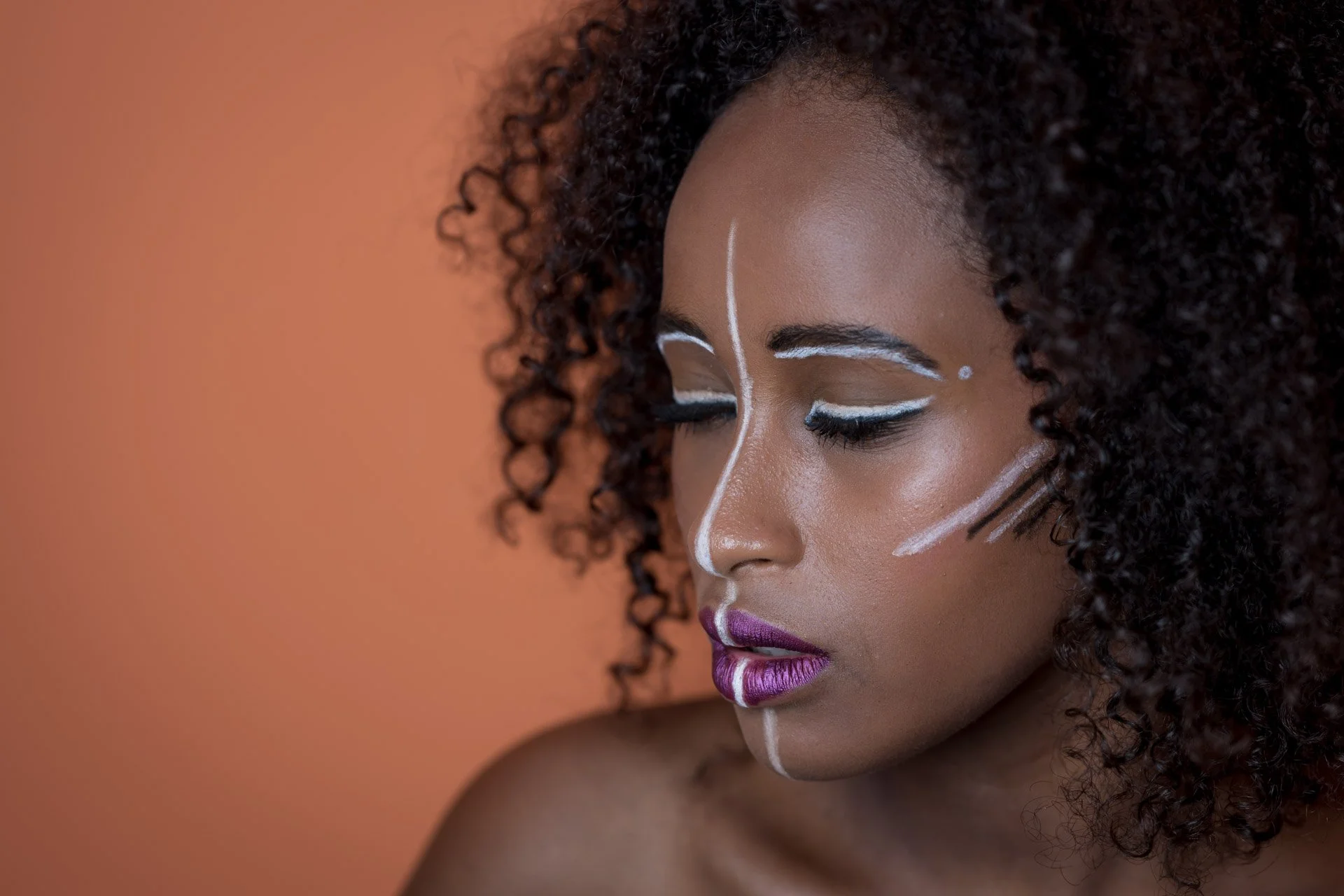 Femme avec du maquillage artistique sur le visage, fond orange.