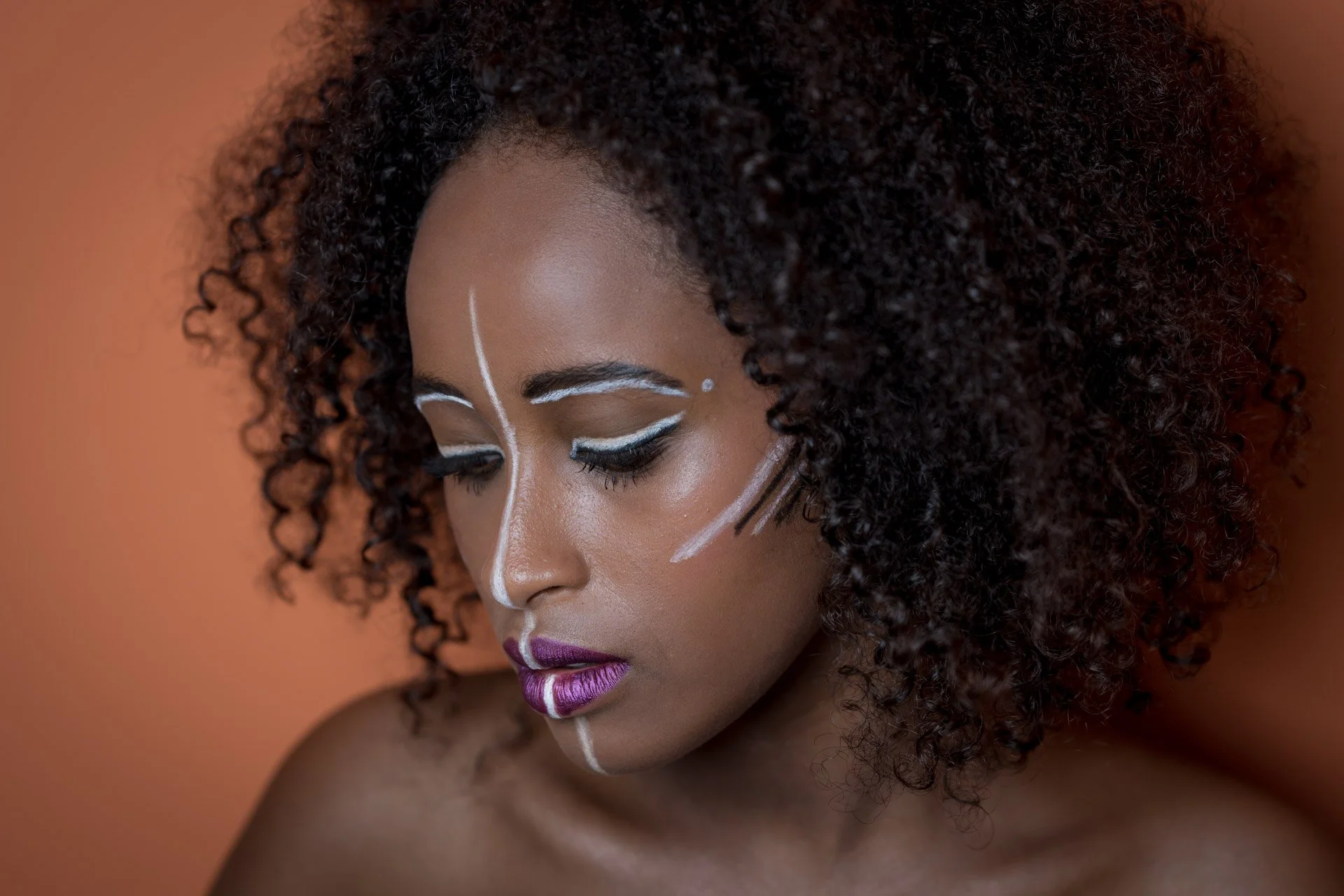 Femme avec maquillage artistique et cheveux bouclés, fond orange.
