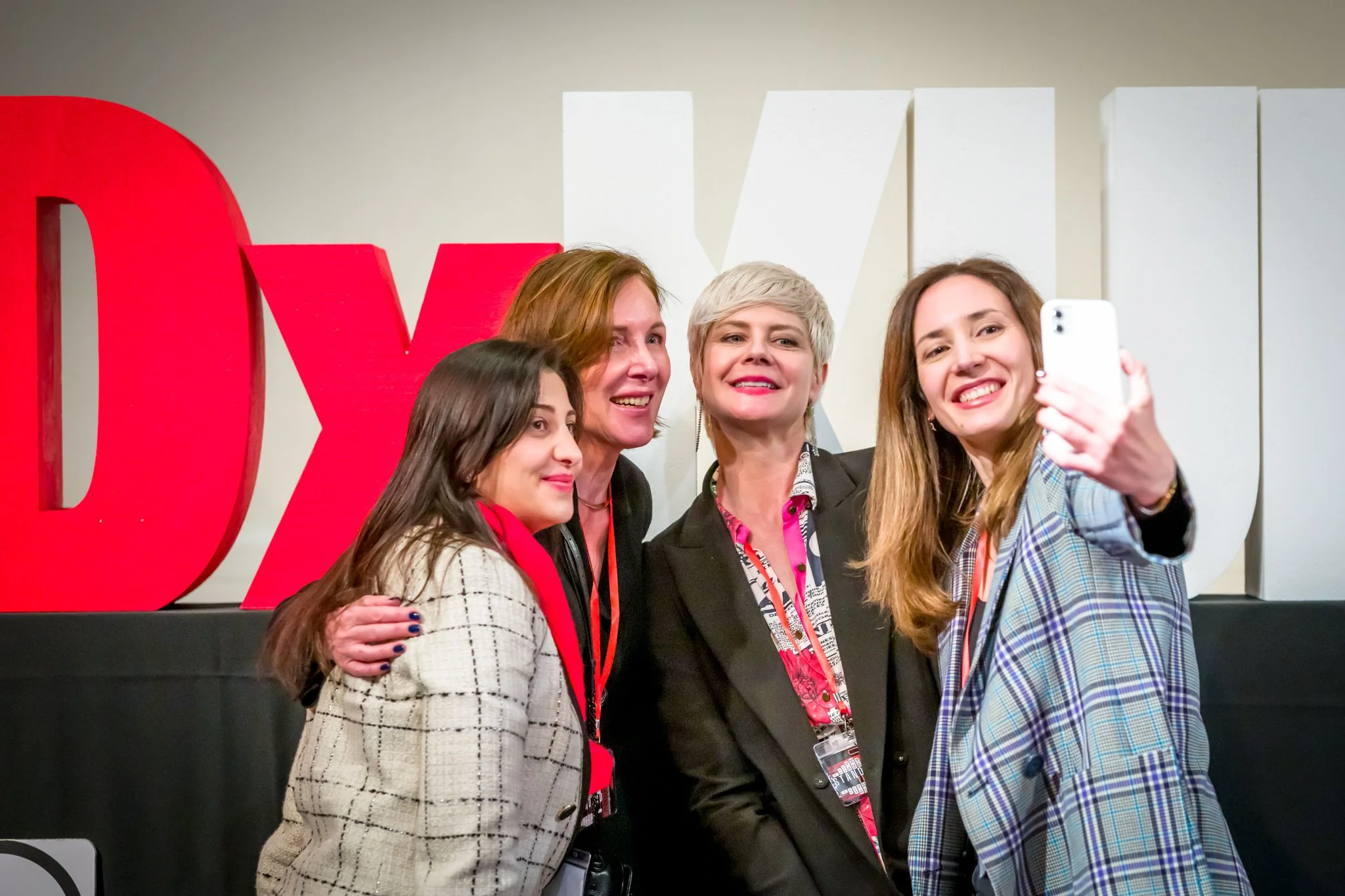 Four women are taking a selfie in front of a TEDx logo.