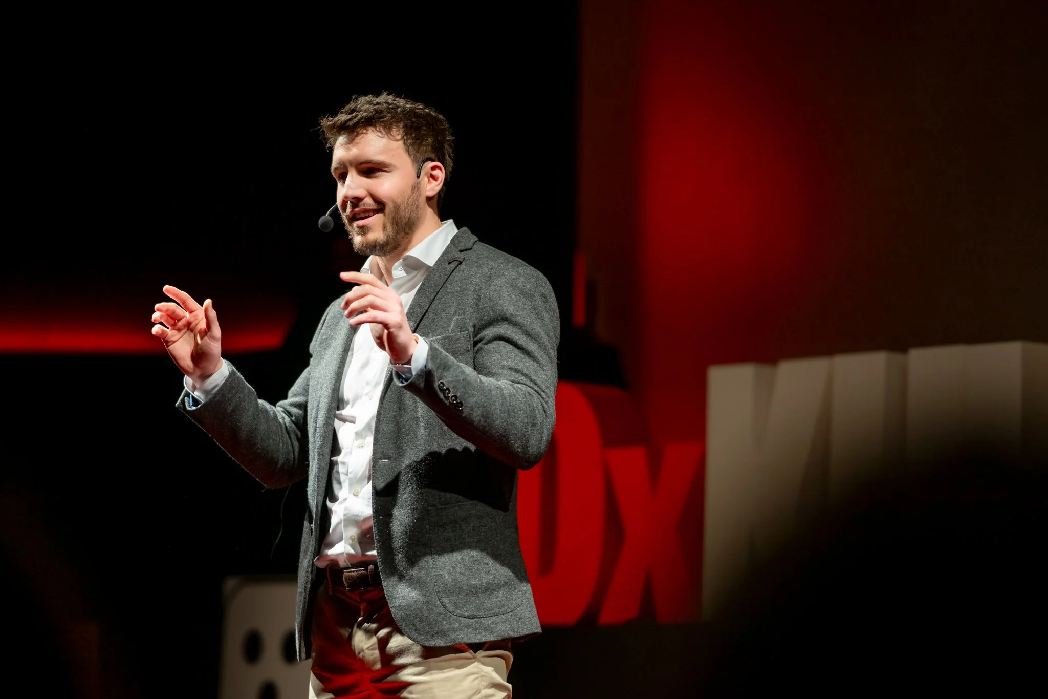 Speaker wearing a headset microphone and gesturing on a TEDx stage.