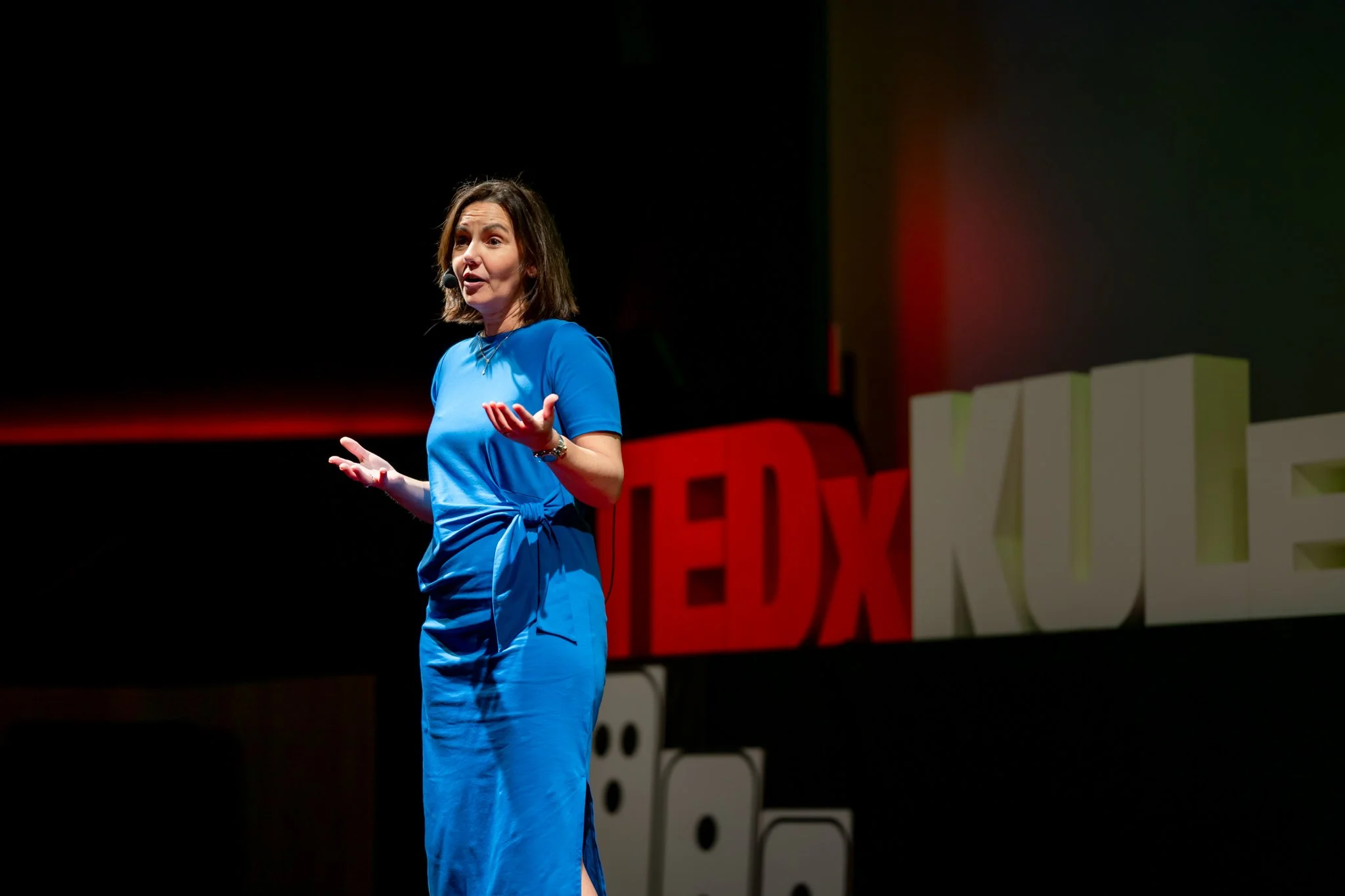 Speaker in a blue dress addressing the audience on a TEDx stage.