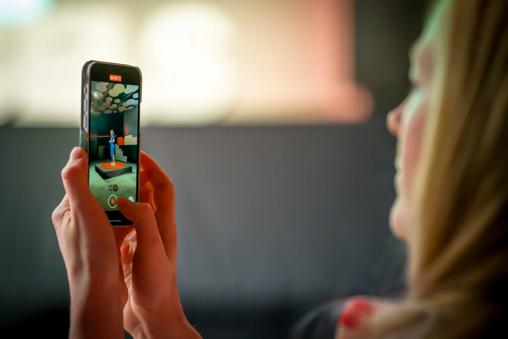 Une femme tient un smartphone en train d'enregistrer une vidéo d'une figure féminine en vitrine.