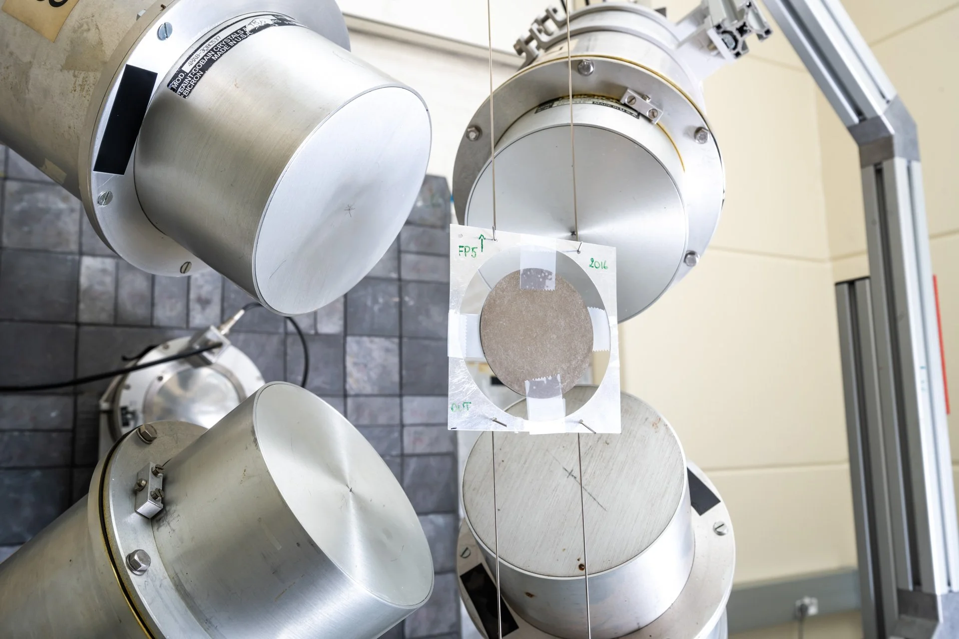 Certains capteurs ou appareils scientifiques métalliques avec un disque en dessous, suspendus par des fils, dans un laboratoire ou une installation scientifique.