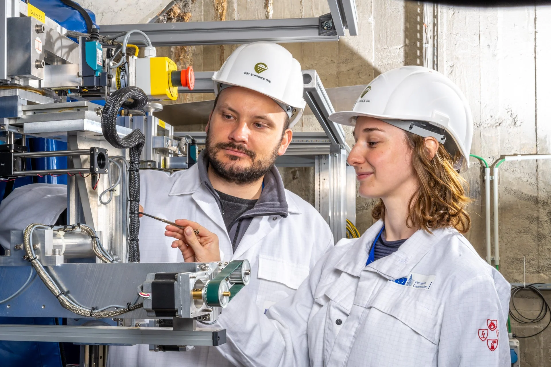 Photo corporate de deux ingénieurs en équipement de sécurité, portant des casques de protection, inspectant des machines industrielles dans une usine.