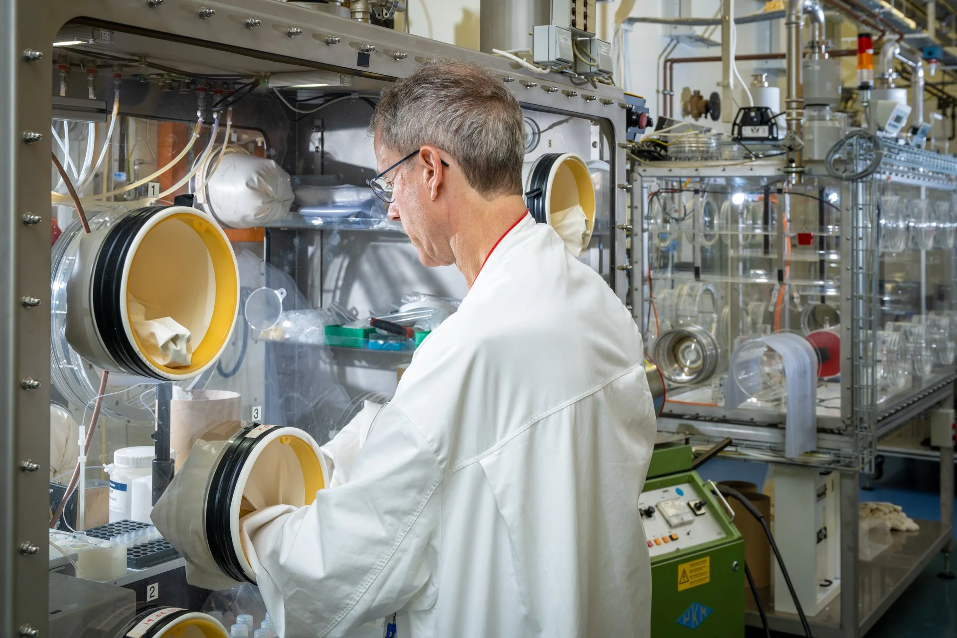 Un scientifique en blouse blanche travaille devant une boîte à gants équipée de deux ouvertures circulaires au JRC à Karlsruhe.