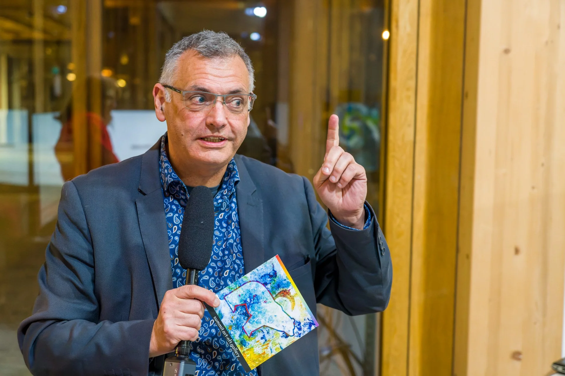 Vincent Parissis présente une illustration bleue et jaune et lève un doigt lors d’une conférence à la BXL ART NFT Gallery.