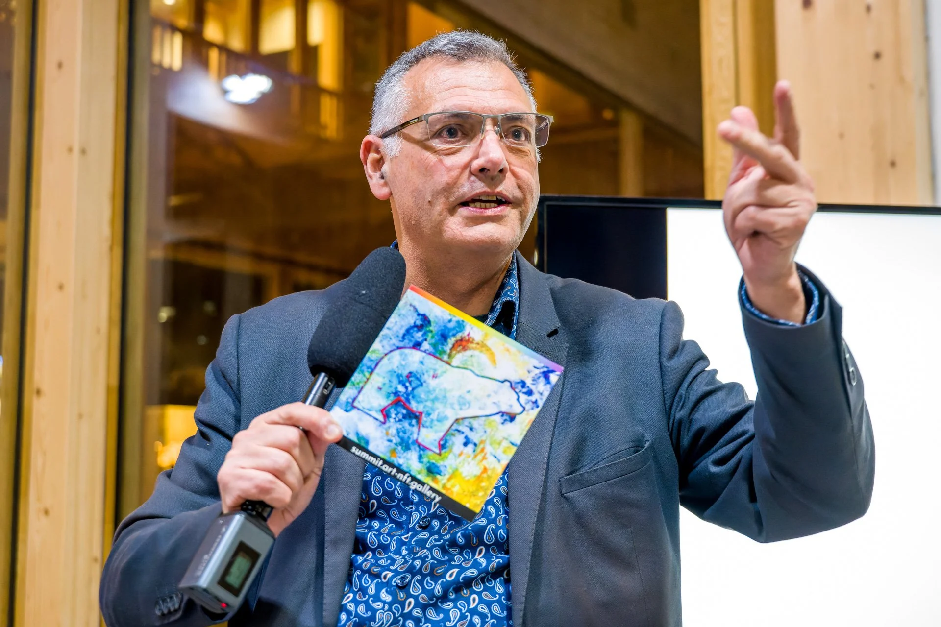 Vincent Parissis tient un microphone et une illustration bleue et jaune, une main levée pour accompagner son intervention.
