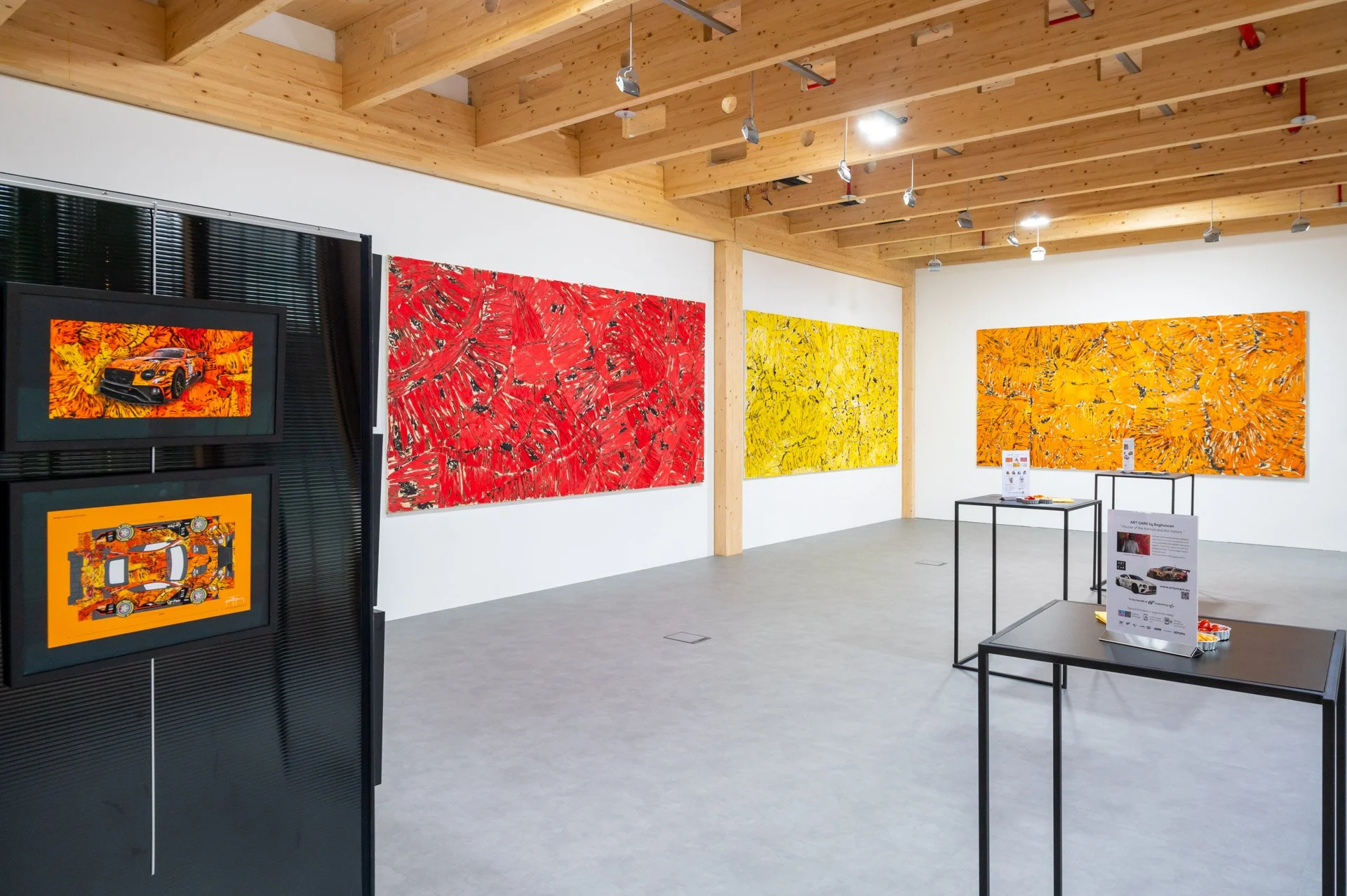 A view of the BXL ART NFT Gallery, with red, yellow and orange paintings on display beneath a wooden ceiling.