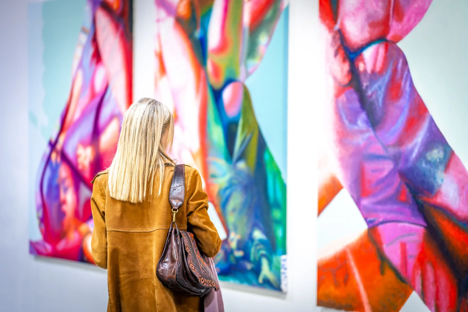 Une femme blonde regarde des peintures abstraites colorées.
