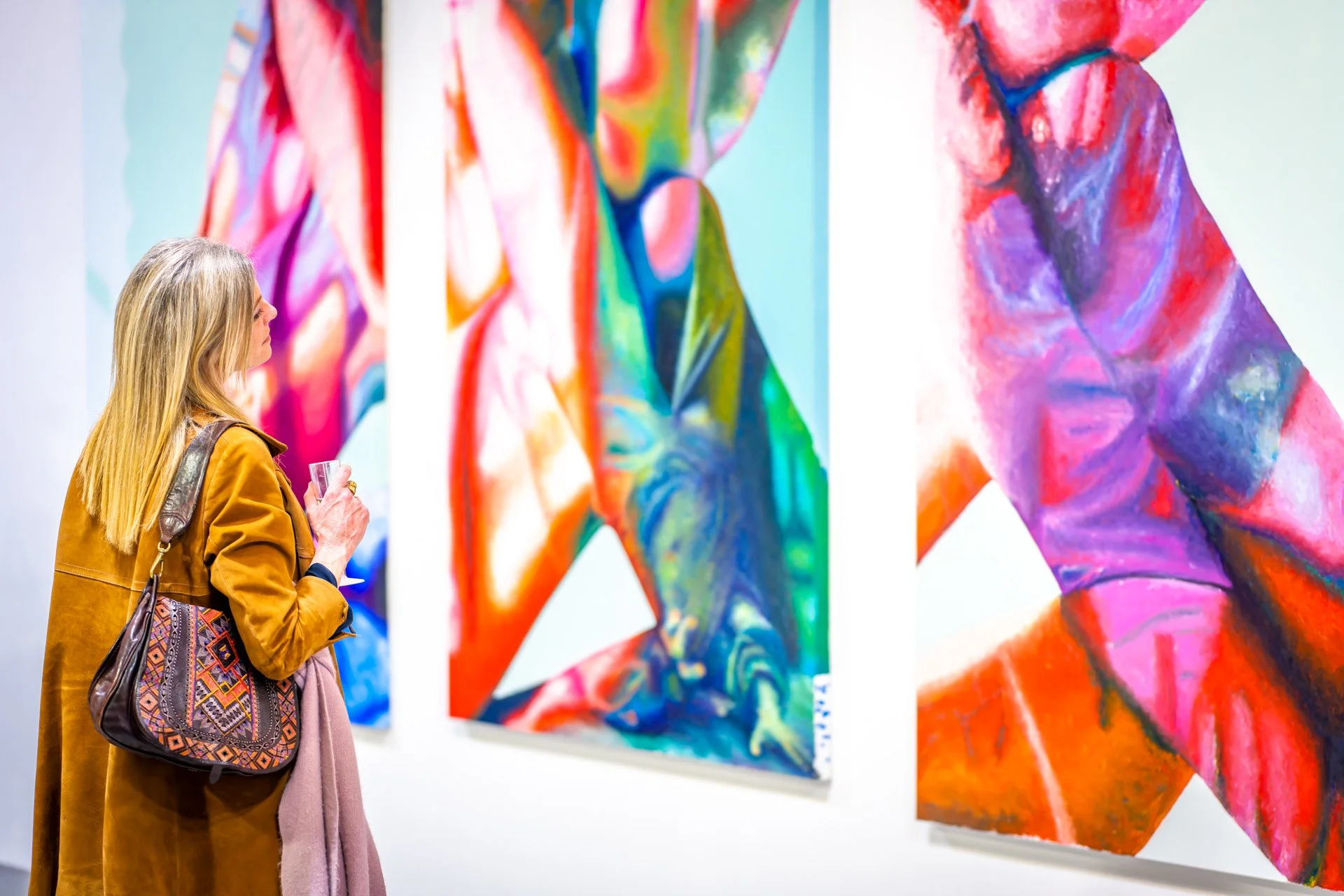 Une femme en manteau marron admire des œuvres d'art abstraites colorées dans une galerie.