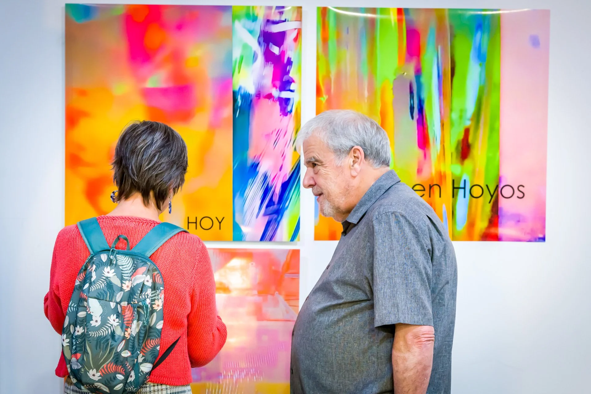 Deux personnes examinent des œuvres d'art colorées dans une galerie.