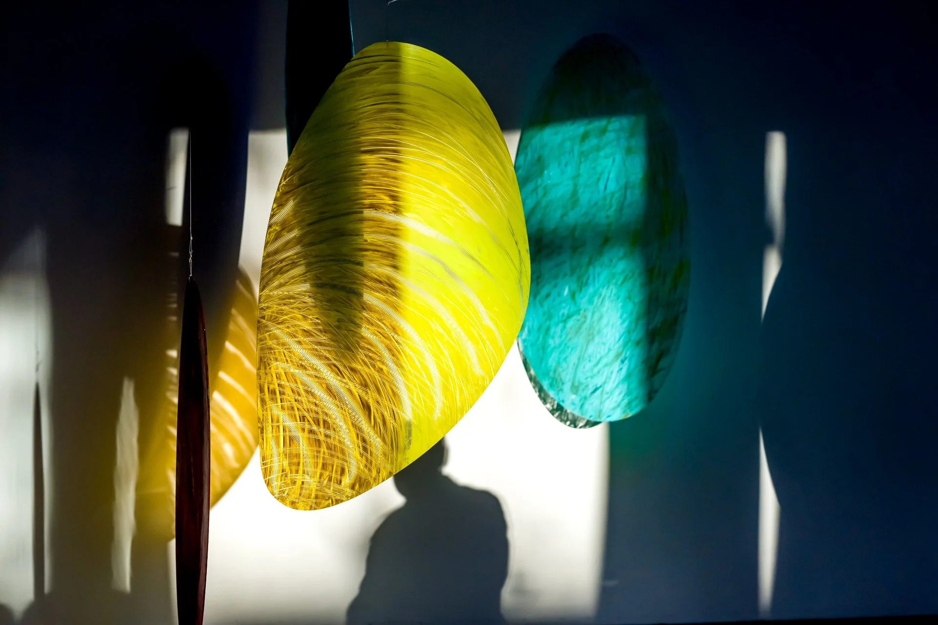 Photographie d'un événement pendant une exposition à Bruxelles. Ombres colorées sur un mur, avec des formes ovales et des couleurs vives comme le jaune et le turquoise, illuminées par la lumière.