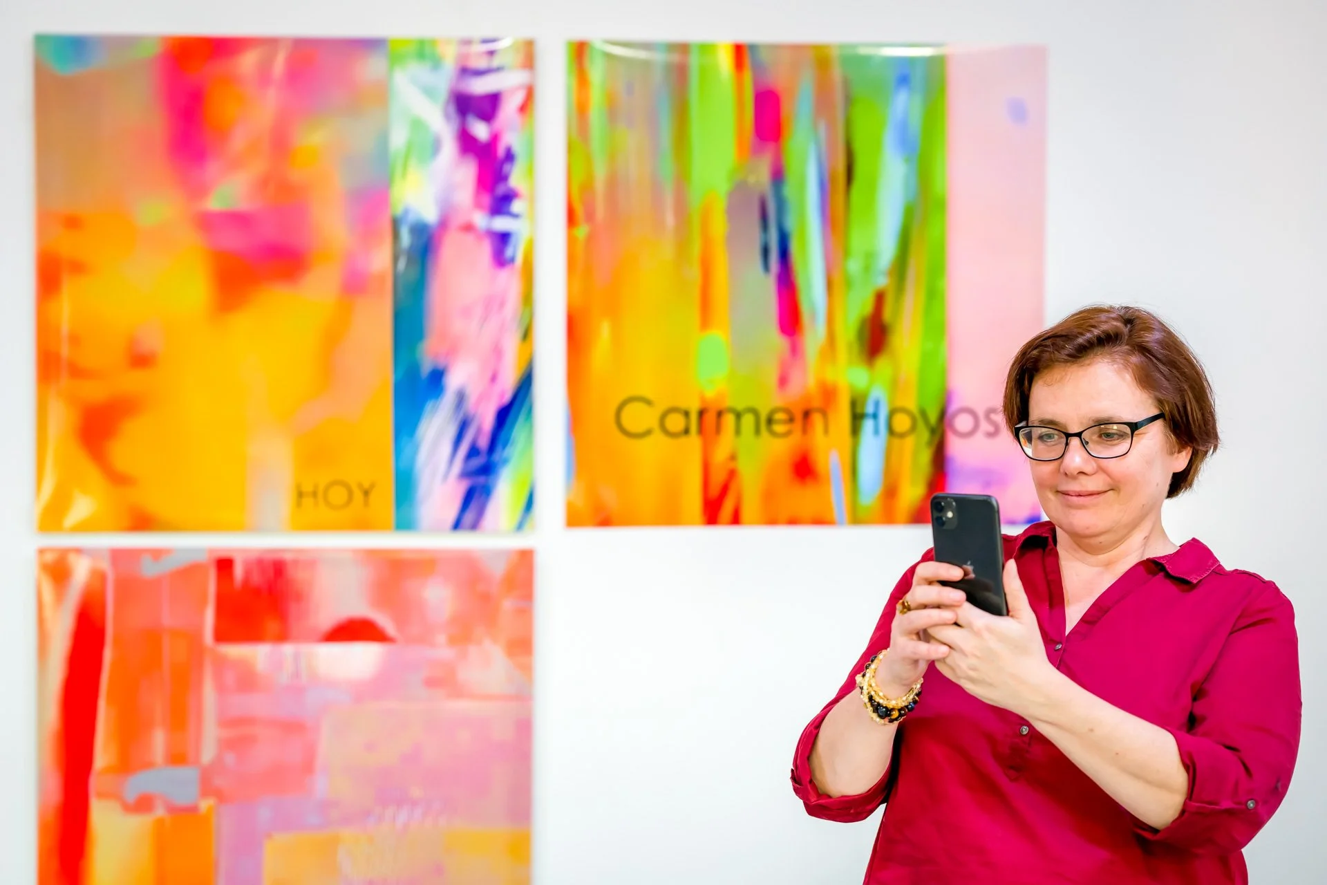Femme prenant une photo avec un téléphone devant des œuvres d'art abstraites colorées accrochées au mur.