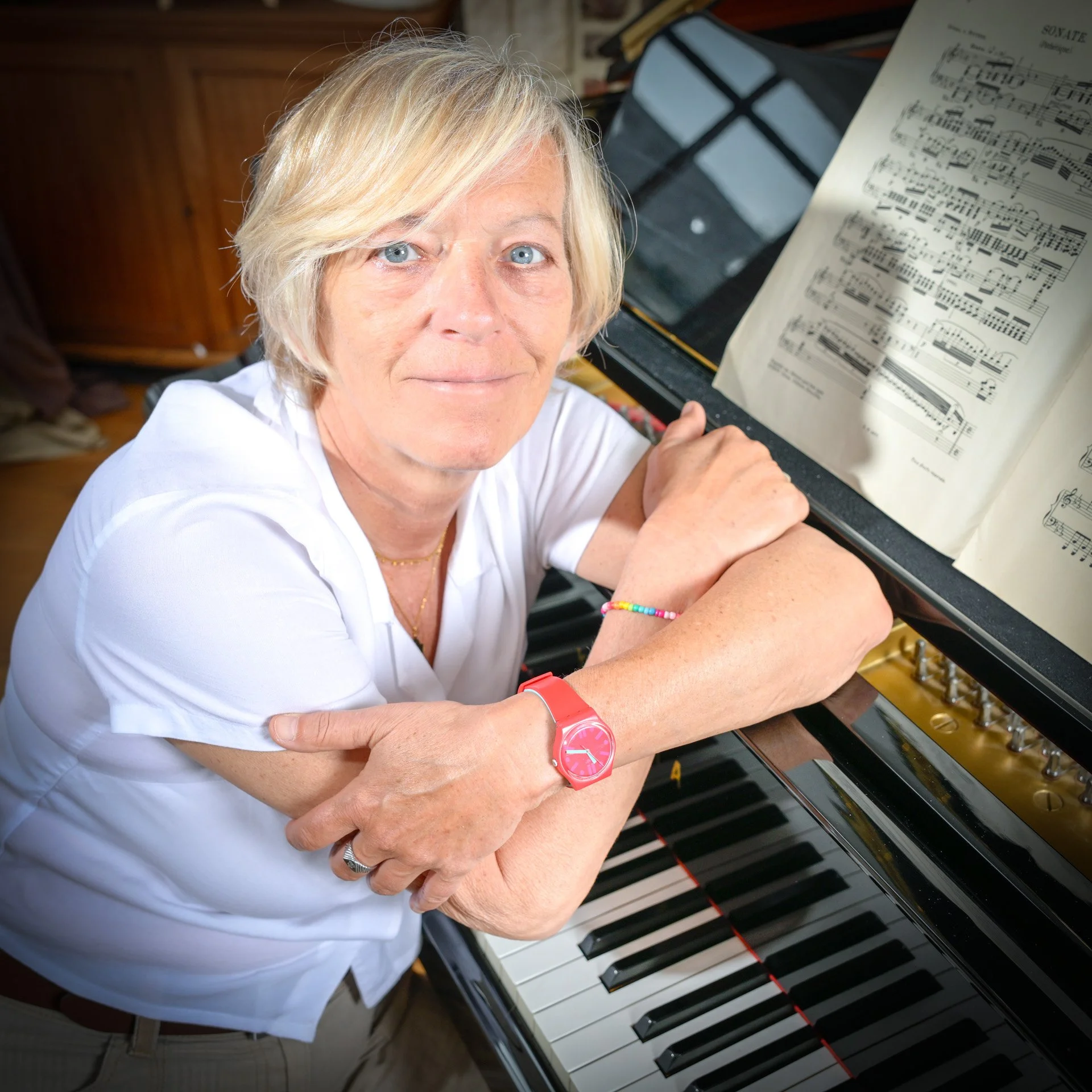 A person leaning on a piano with a sheet of music open, wearing a pink watch.