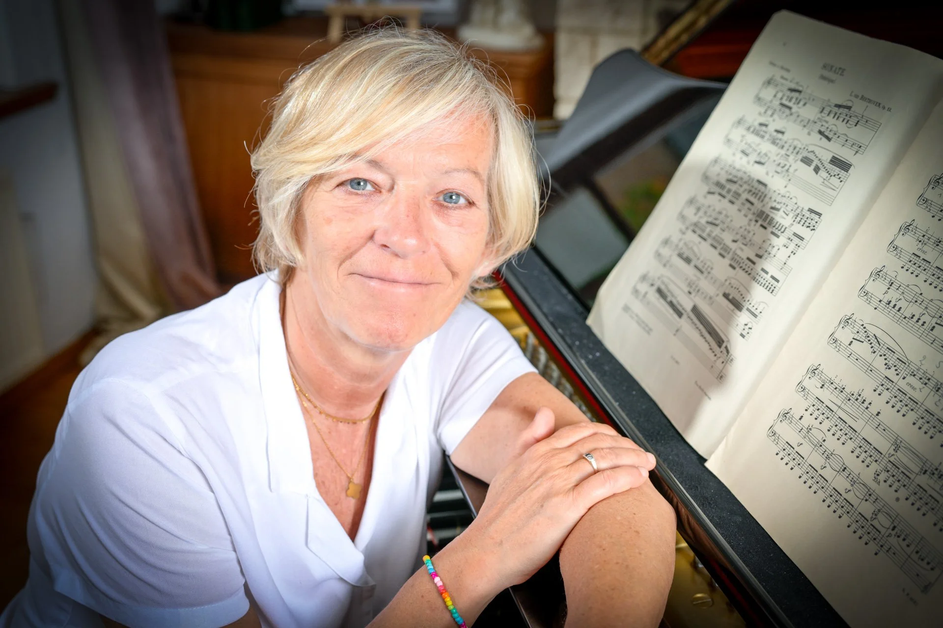 A blonde woman standing next to a piano with sheet music on the music stand.
