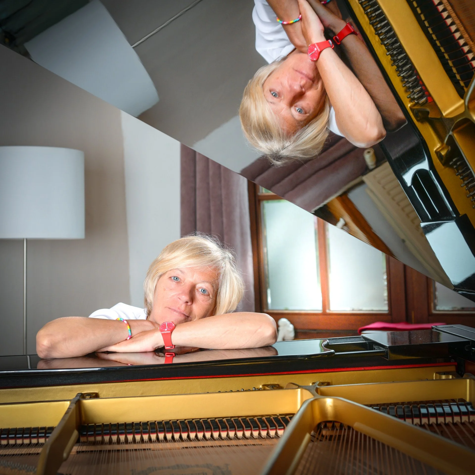 A person lying on a grand piano, reflected in the open lid. The interior of the house is visible.