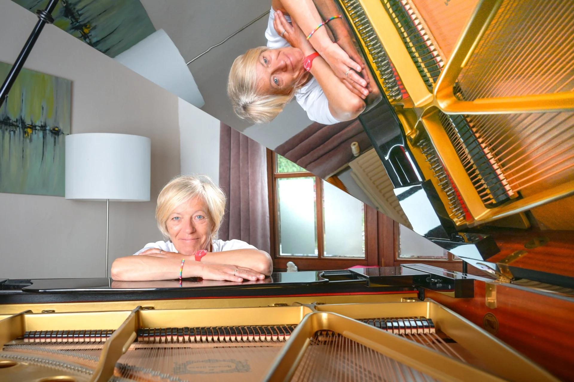 Fabienne Vignier pose derrière un piano à queue ouvert, avec son reflet visible dans le couvercle.