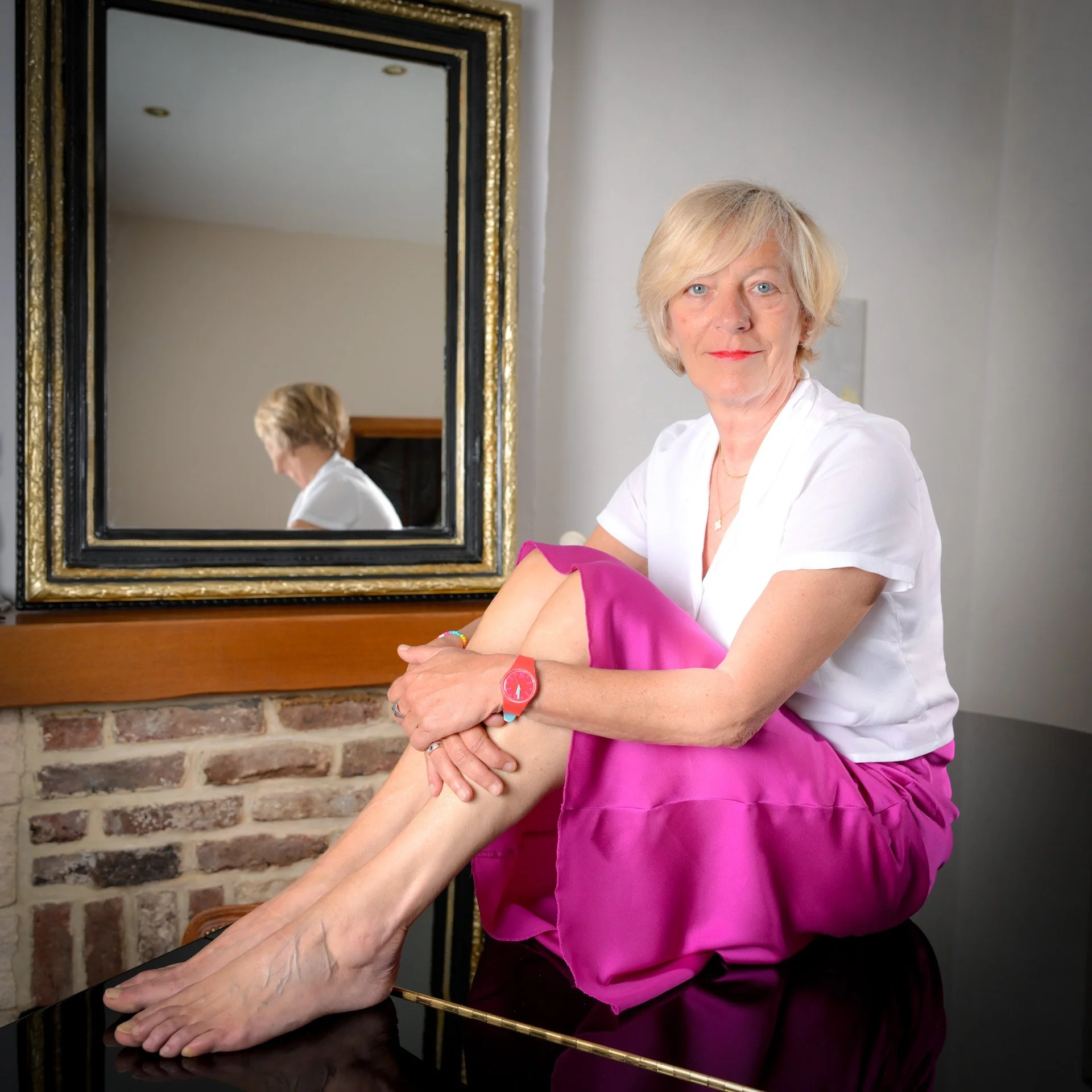 A person sitting down, wearing a pink skirt and a white blouse, in front of a mirror.