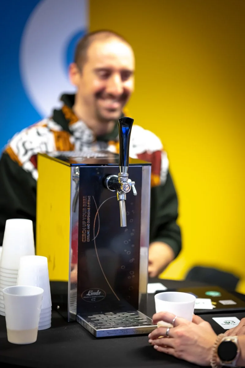 Un participant souriant derrière une borne de distribution de boissons Self Bar lors du meetup WalChain à Charleroi.
