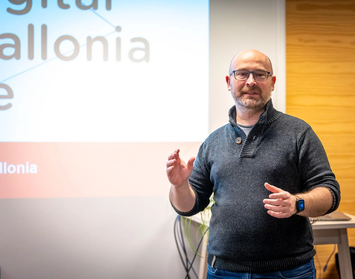 Denys Bornauw accompagne son intervention d’un geste de la main devant un écran Digital Wallonia lors du meetup WalChain à Charleroi.