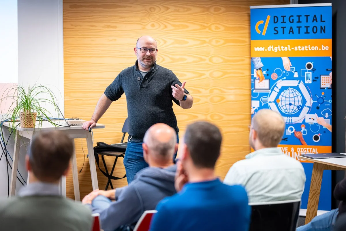 Denys Bornauw s’adresse à un public assis, près d’une bannière Digital Station, lors du meetup WalChain à Charleroi.