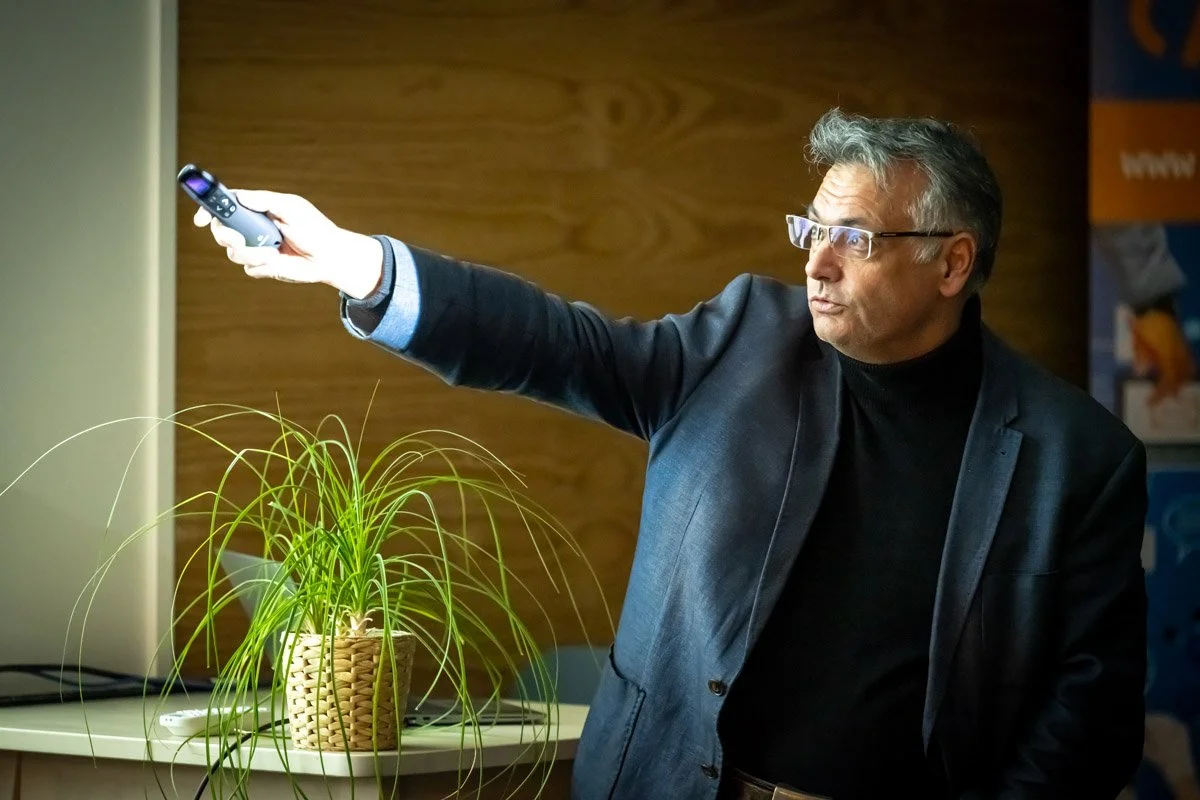 Vincent Parissis tend le bras avec une télécommande pour désigner l’écran lors du meetup WalChain à Charleroi.