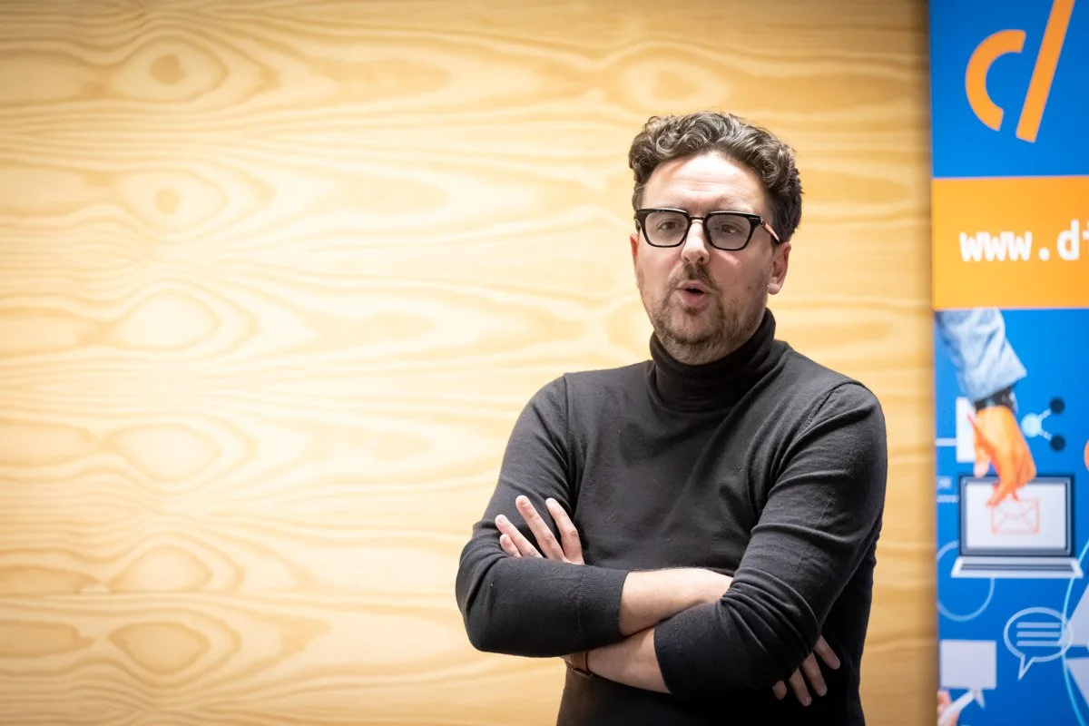 Thomas Parmentier, en pull sombre et lunettes, écoute les bras croisés lors du meetup WalChain à Charleroi.