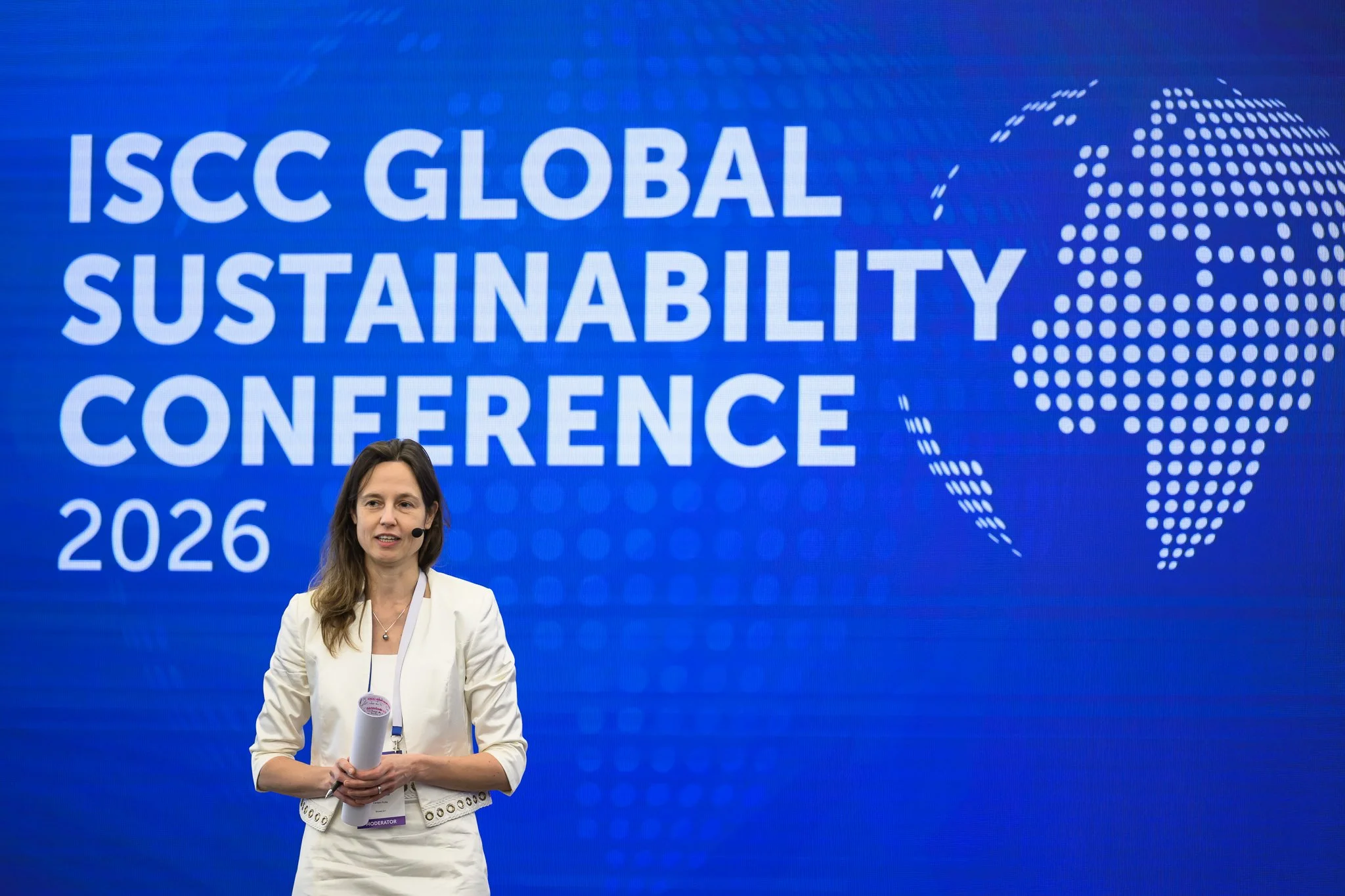 A woman addresses the audience in front of the ISCC Global Sustainability Conference 2026 backdrop.
