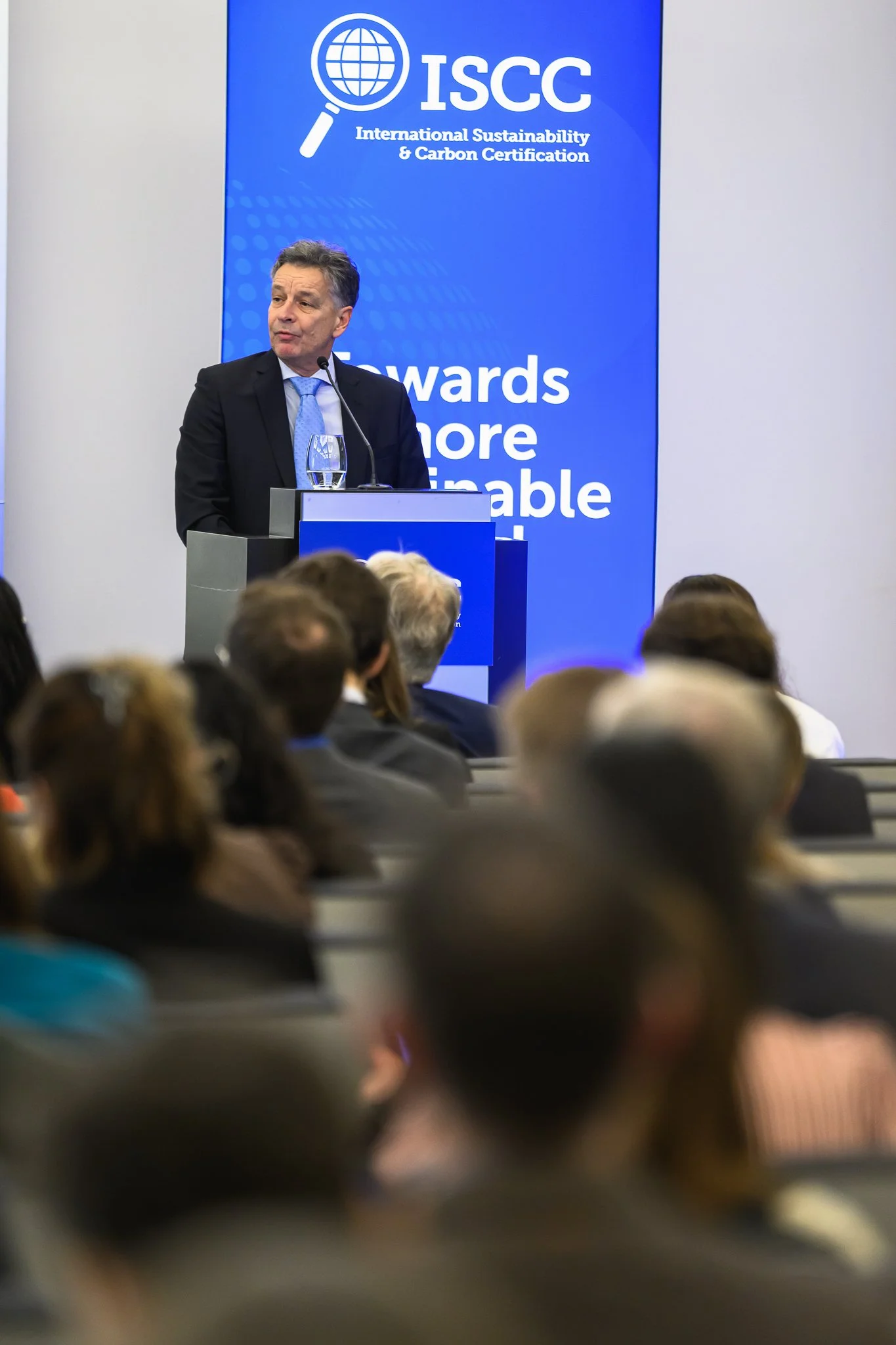 A man addresses the audience from a lectern beside an ISCC banner.