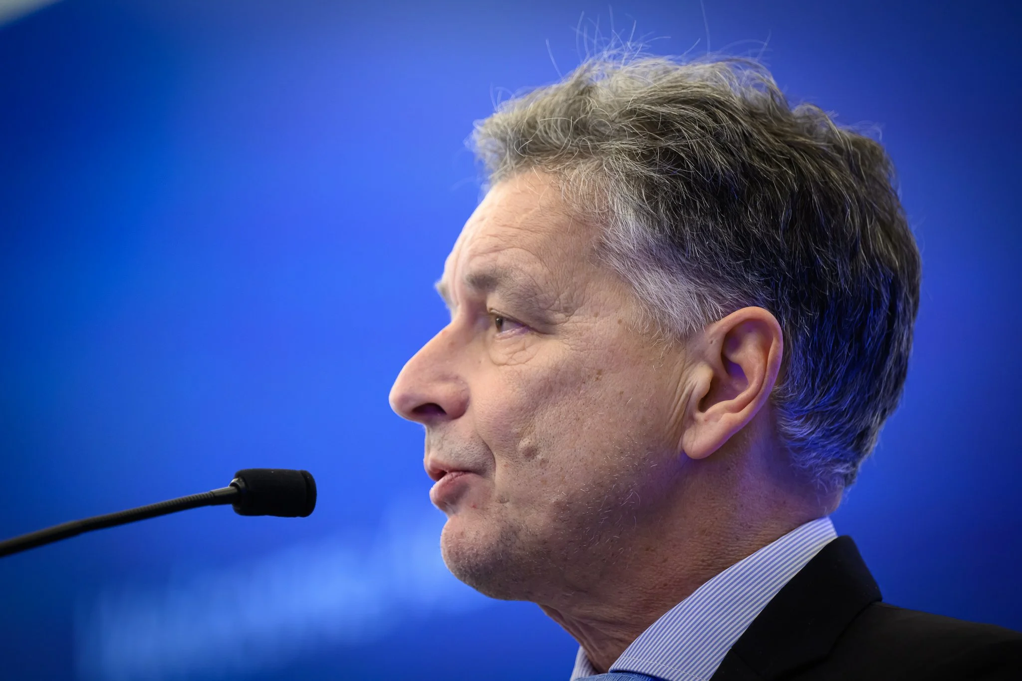 Close-up profile of a man speaking against a blue conference backdrop.