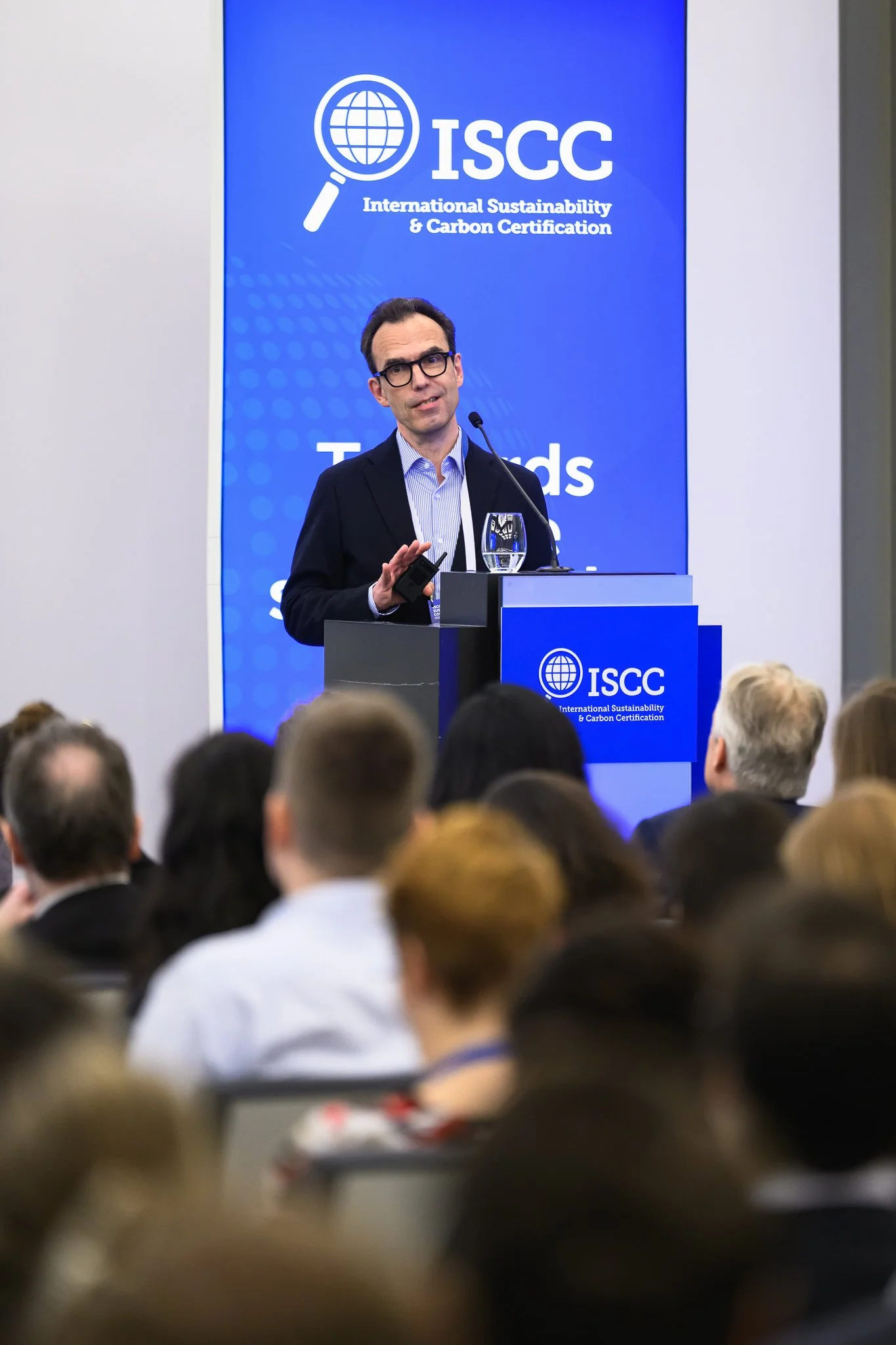 A man with glasses addresses the audience from a lectern.