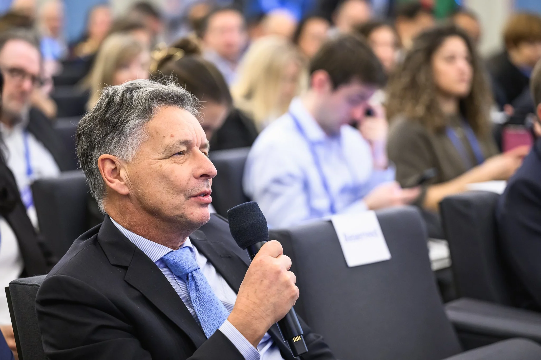 A man in the audience asks a question using a handheld microphone.