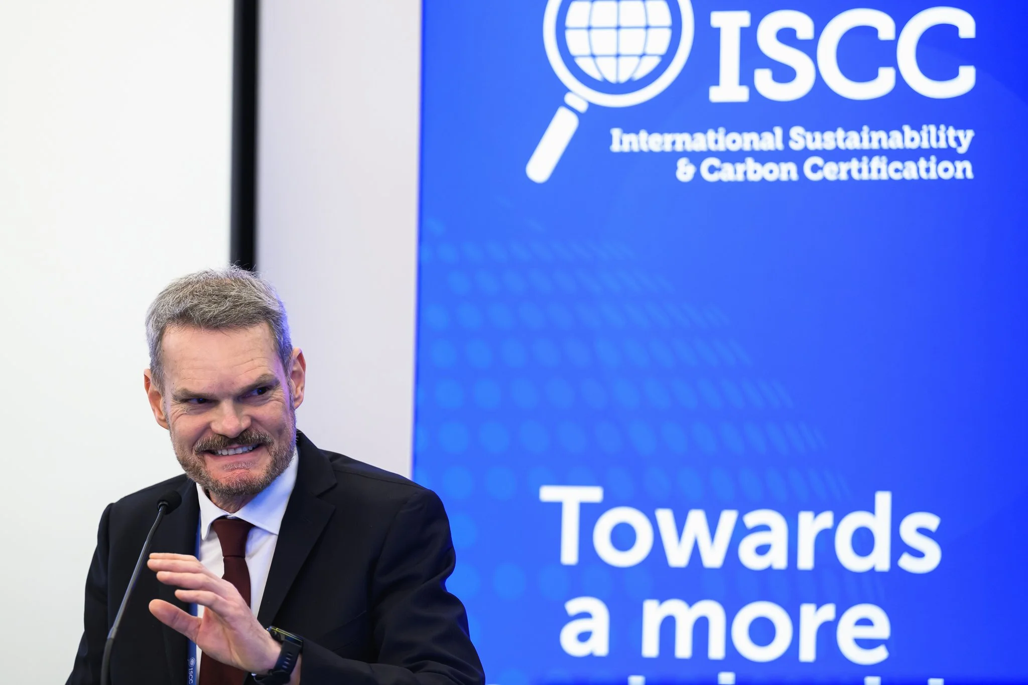 A bearded man smiles at the lectern beside the ISCC logo.