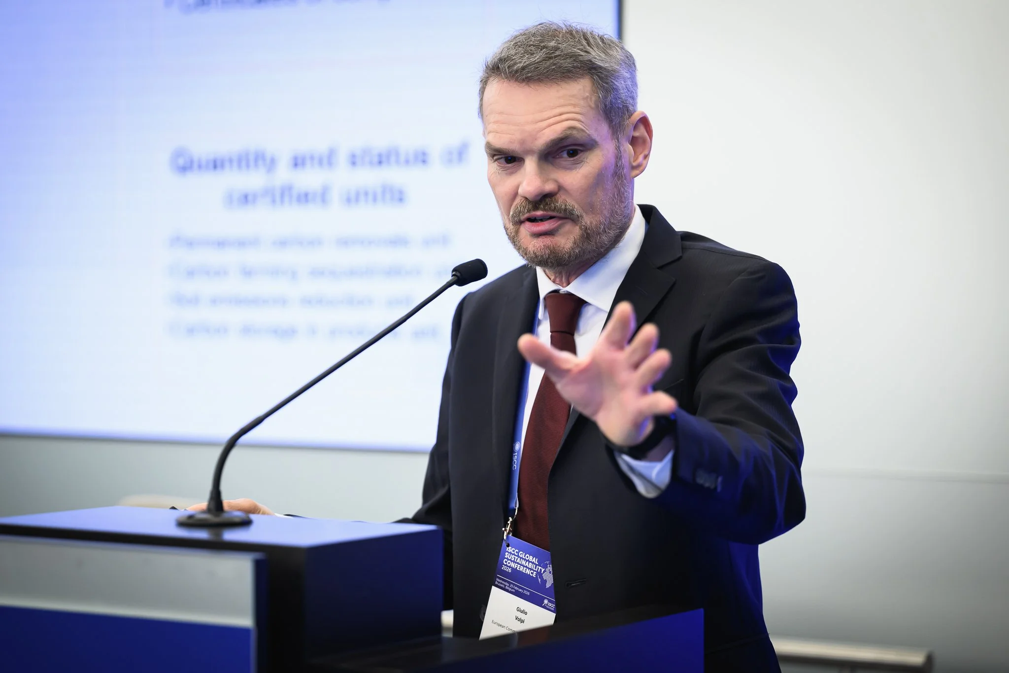 A bearded speaker extends his hand towards the audience during a presentation.