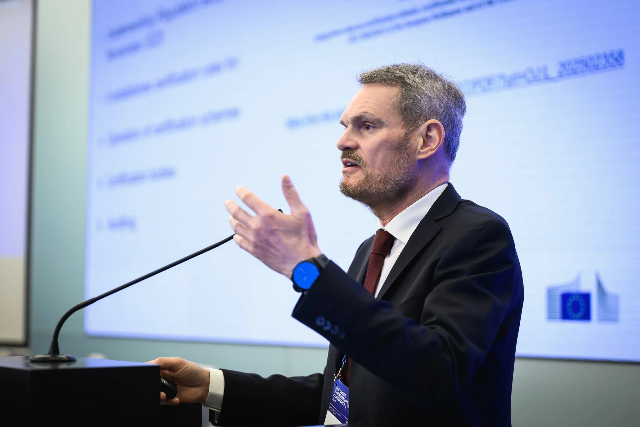 A bearded man gestures while speaking at the lectern.