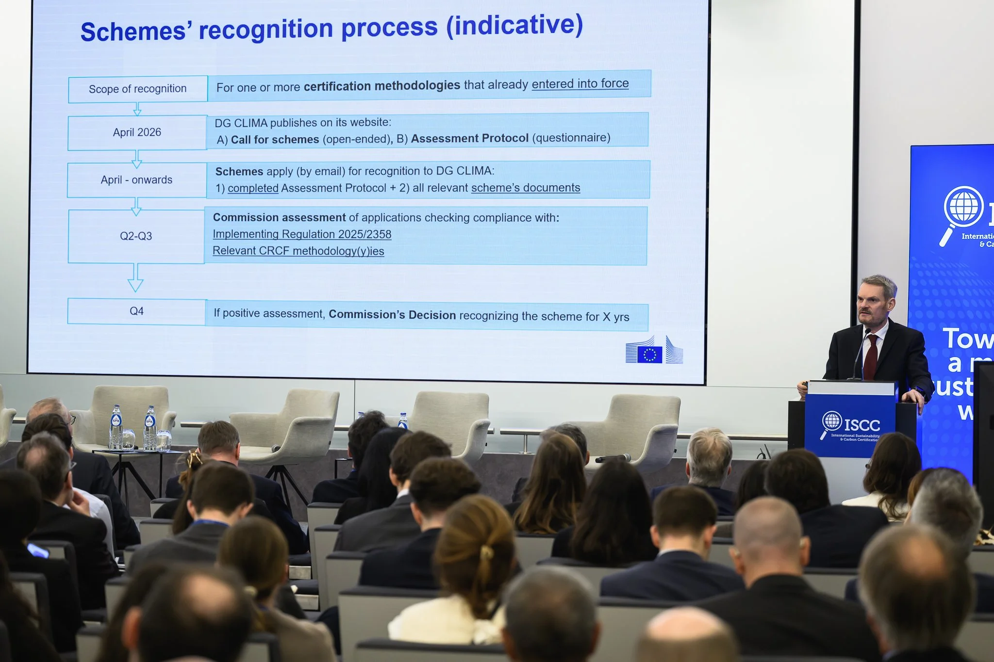 The audience watches a presentation slide about the recognition process for certification schemes.