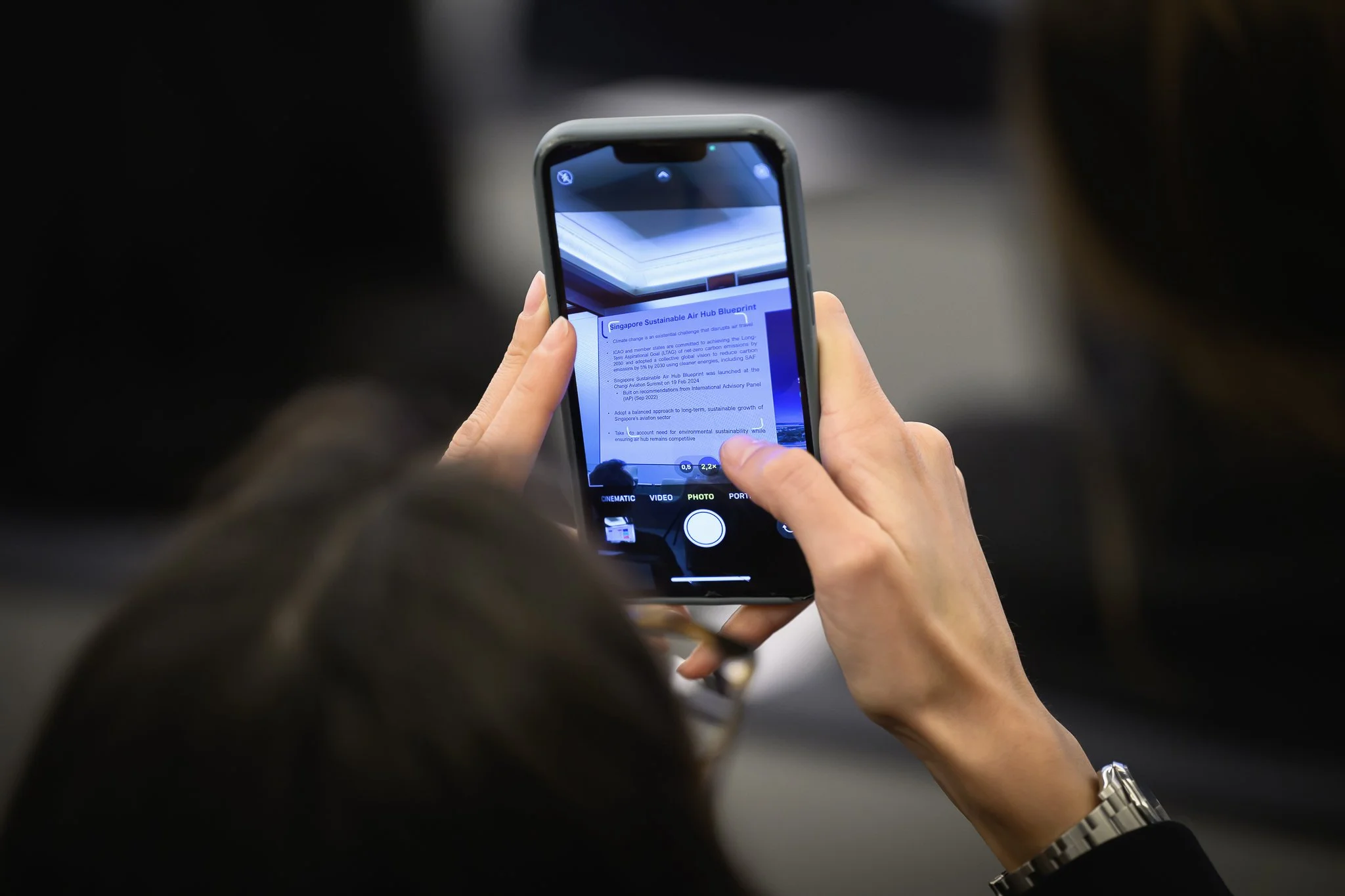 An audience member uses a smartphone to photograph a projected presentation slide.