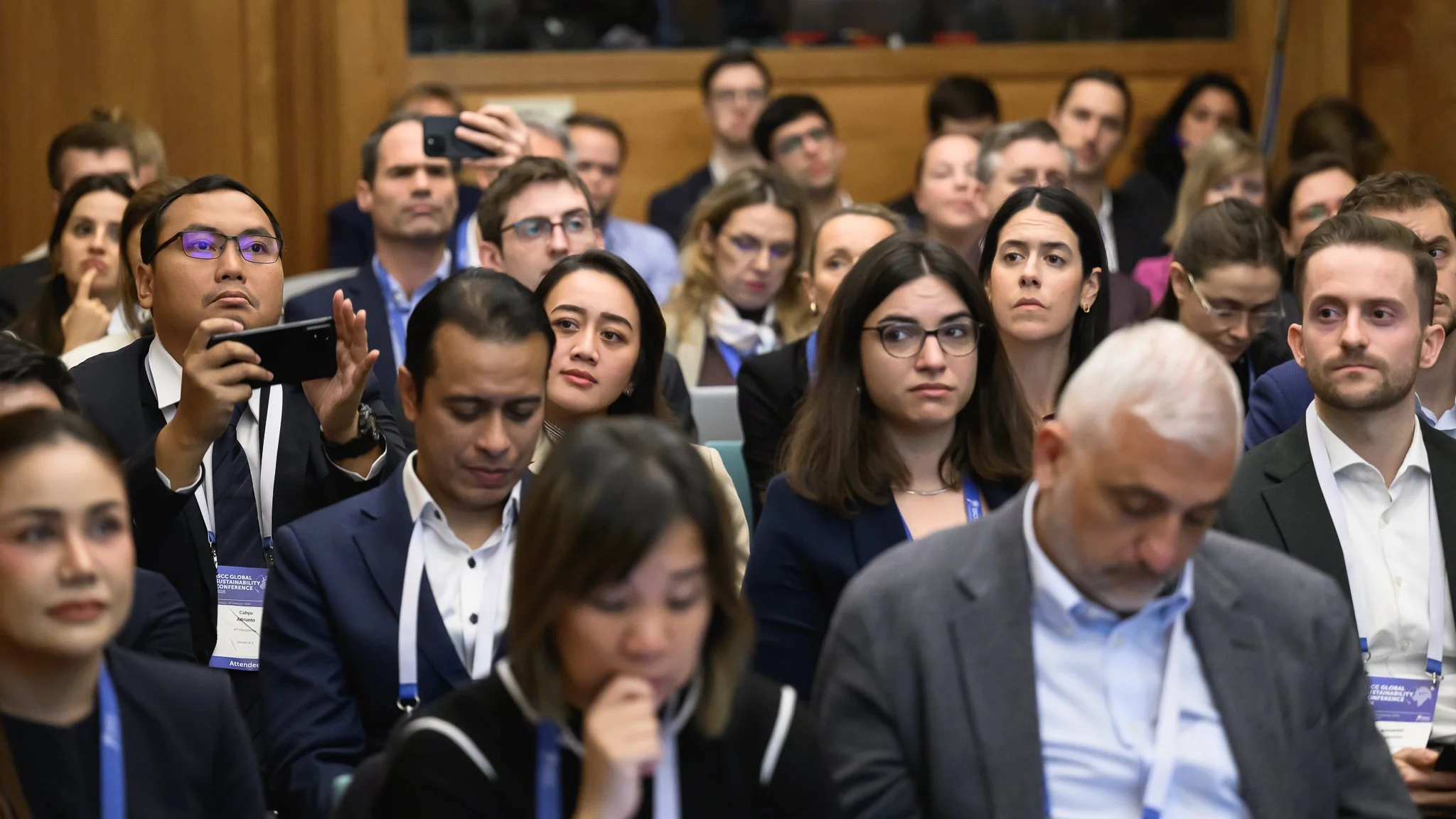 Rows of conference participants listen attentively in a wood-panelled room.